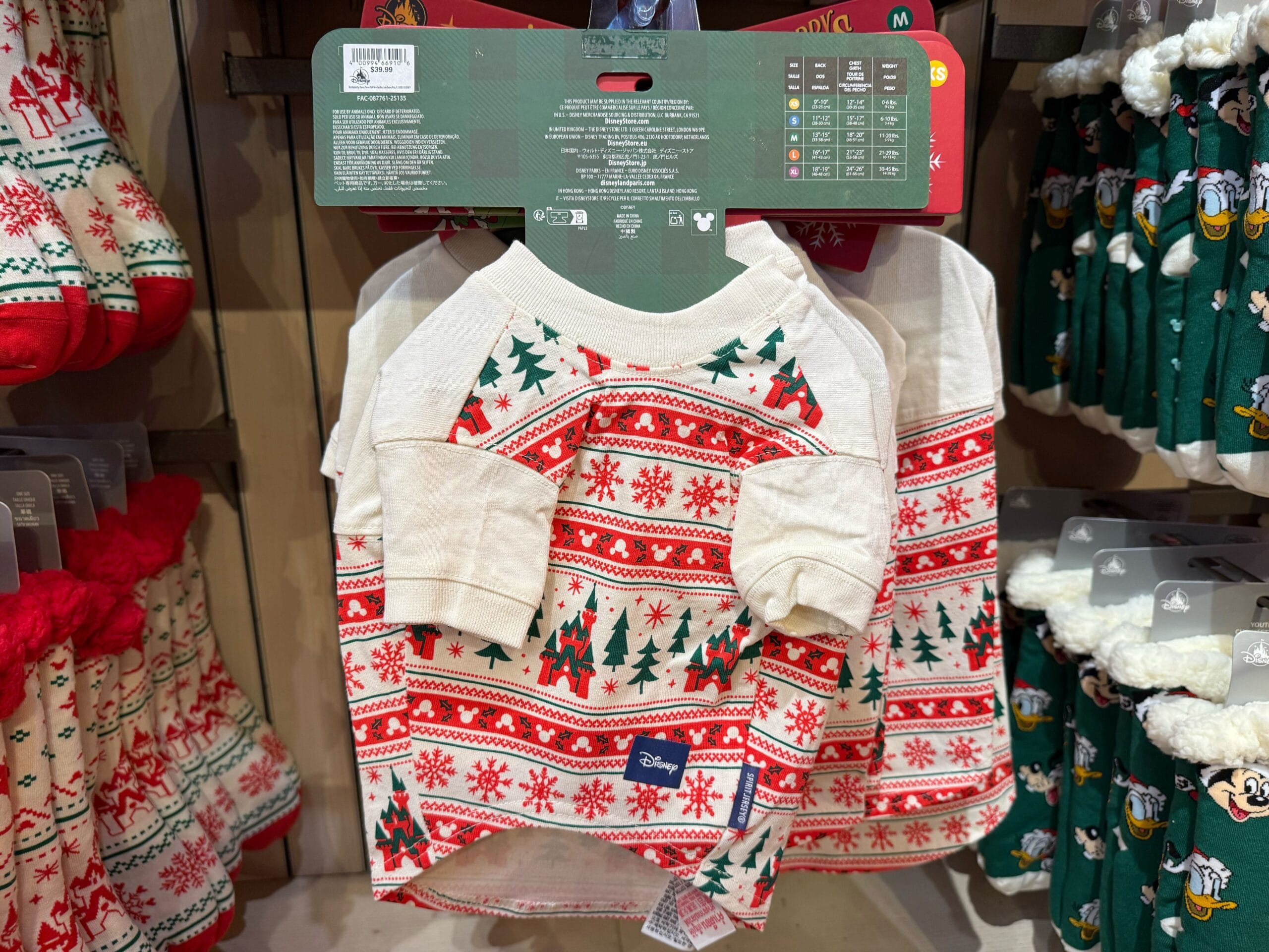 A festive red, white, and green Peppermint Collection pet sweater with snowflakes and trees on display at a Disney park store.