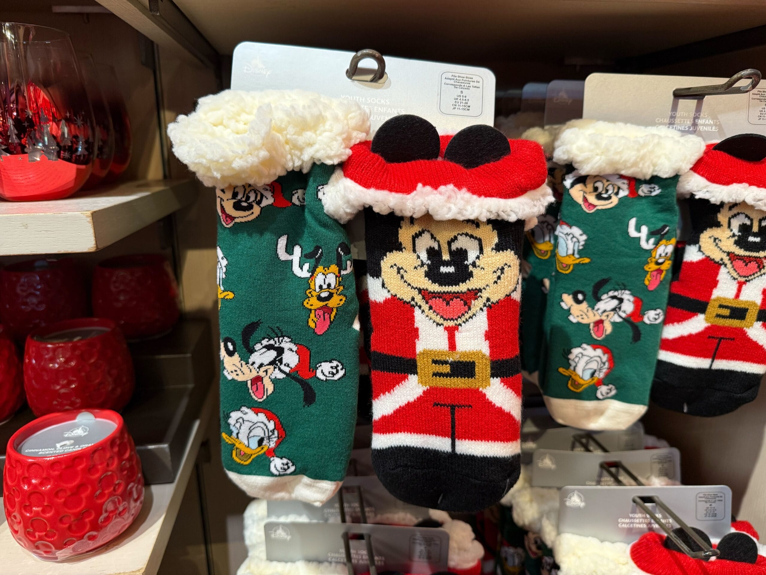 Colorful Christmas socks featuring Mickey Mouse and friends sit with Disneyland holiday merchandise beside candles on a festive shelf.