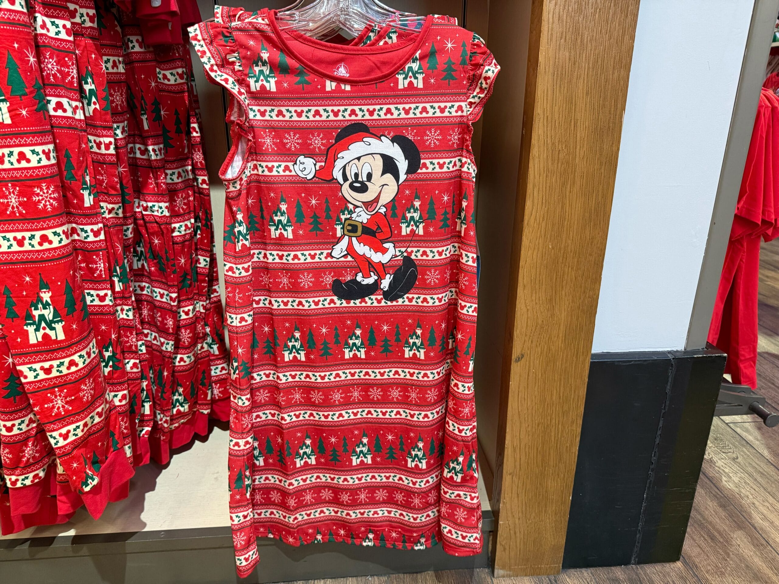 Red Christmas dress featuring Mickey Mouse in a Santa outfit, part of Disneyland holiday merchandise, no castle in view to compare.
