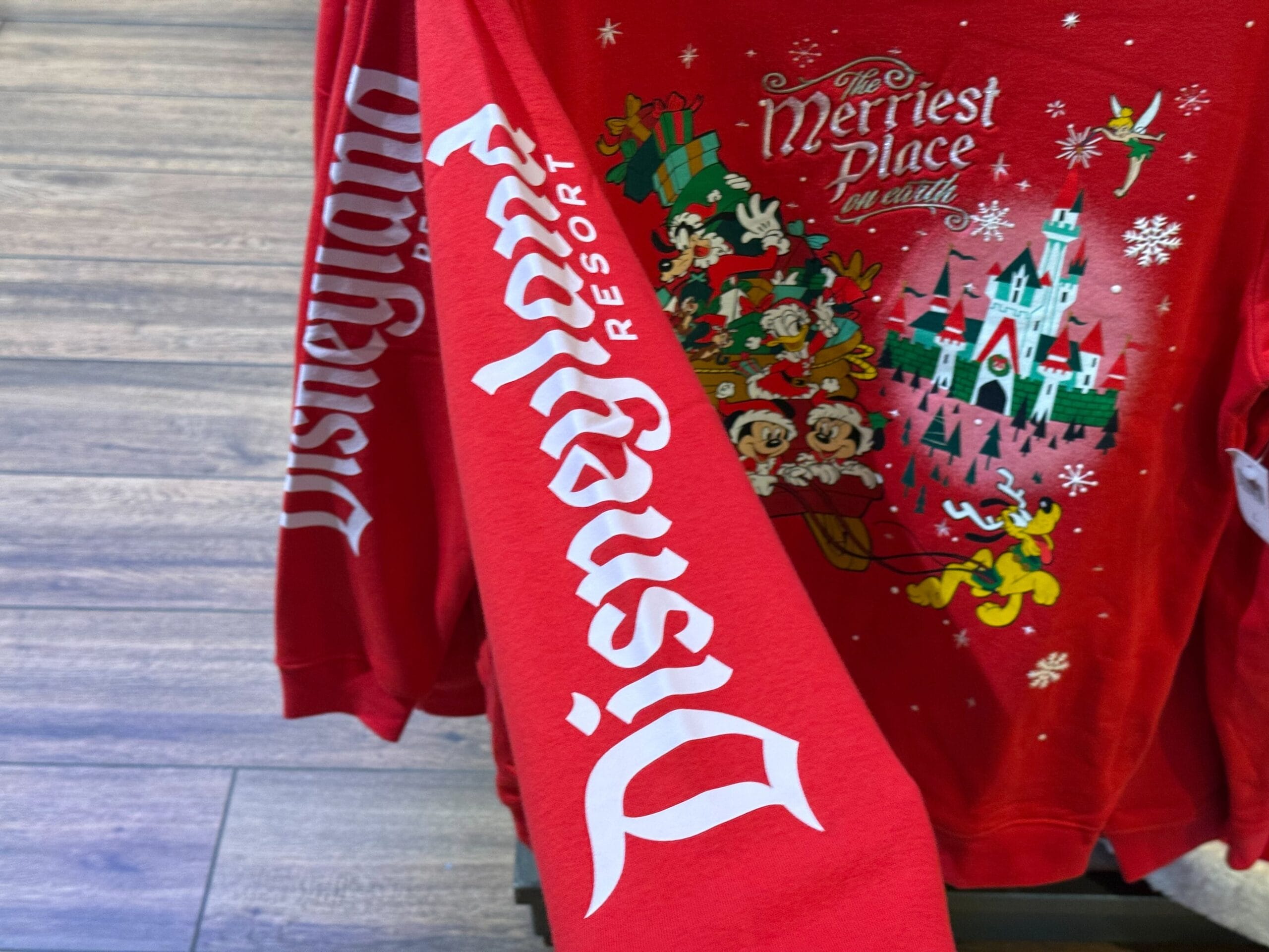 Red Disneyland Christmas sweater featuring Sleeping Beauty Castle, Disney characters, and "The Merriest Place on Earth" design.