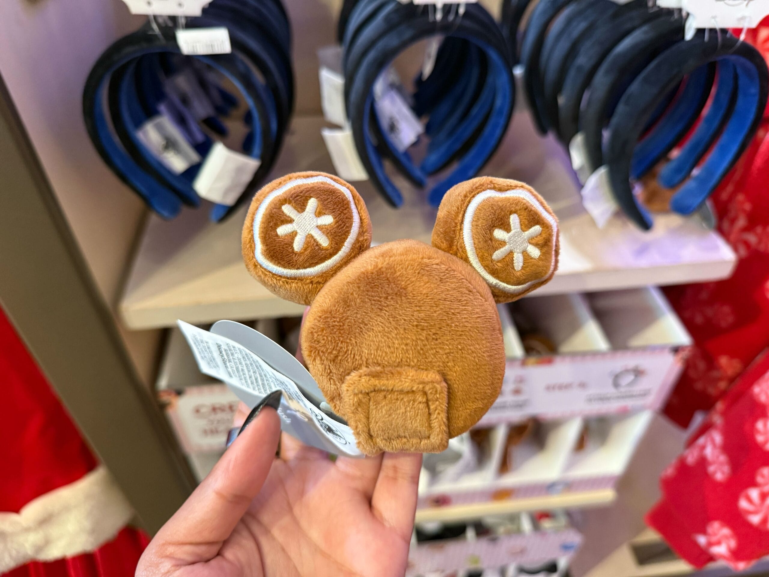 A hand holds a plush brown Mickey Mouse ear hair clip from the Disneyland Christmas collection, reminiscent of festive park merch.