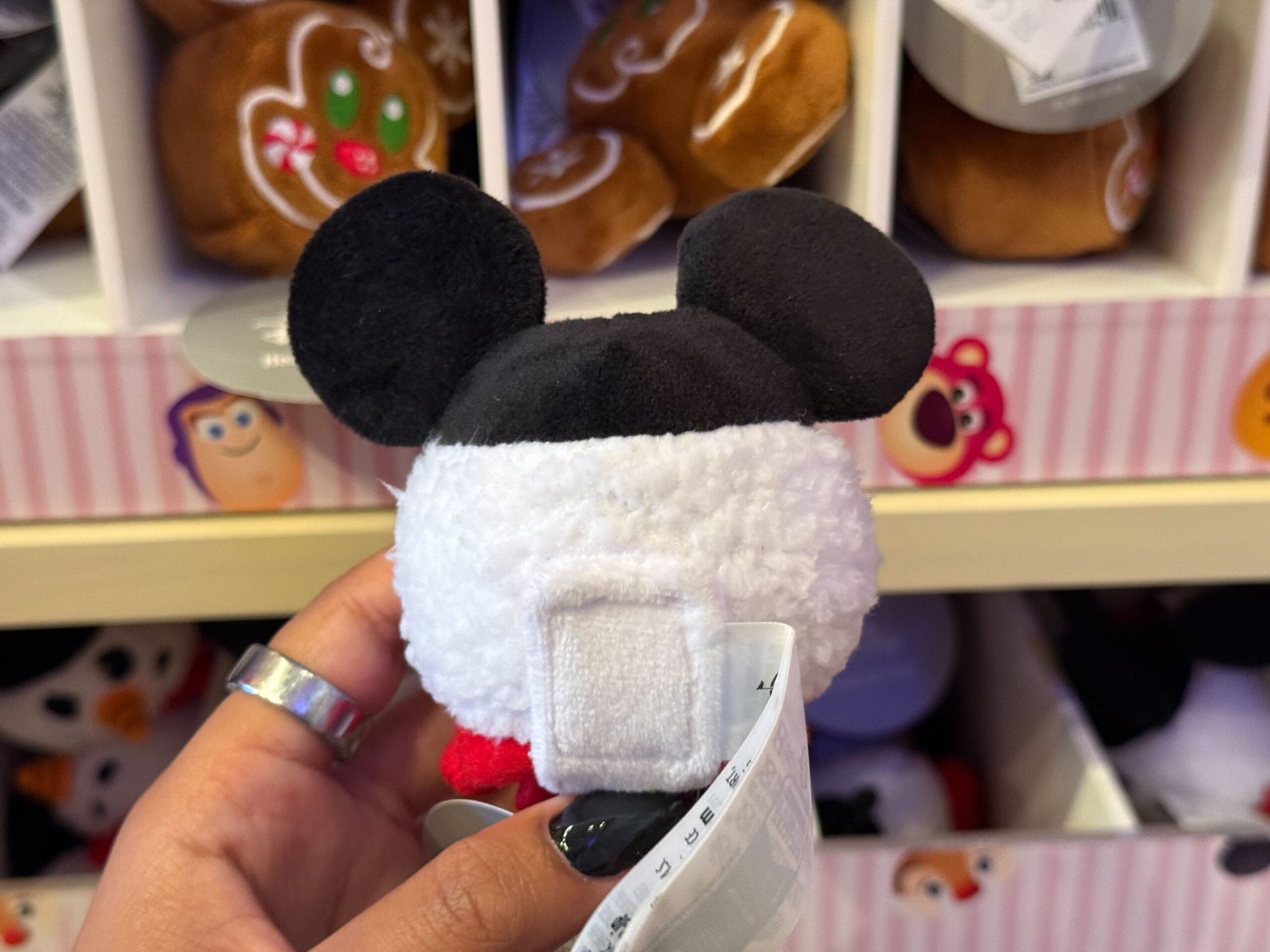 A hand holds a small plush toy with black mouse ears from Disneyland’s Christmas collection, evoking classic park merchandise style.