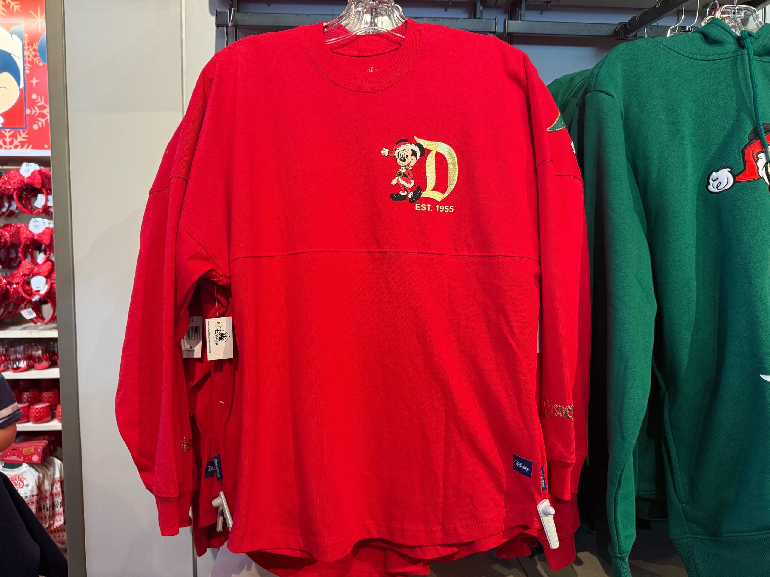 Red Disneyland Christmas shirt with festive Mickey Mouse and gold "D" logo, reminiscent of Anaheim's Sleeping Beauty Castle style.