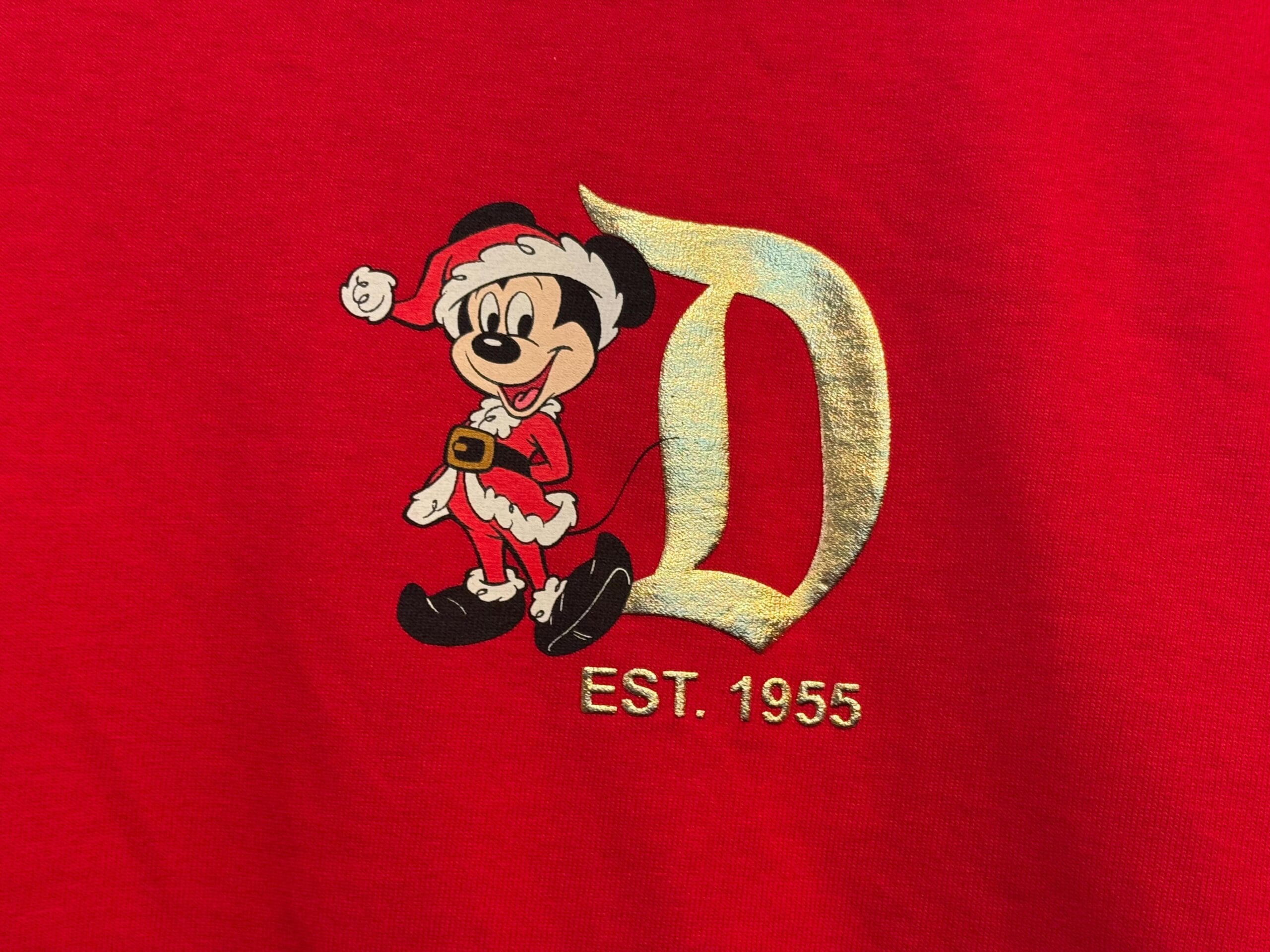 Mickey Mouse in a Santa outfit stands by a gold "D"—classic Disneyland holiday style, reminiscent of the California park’s red décor.