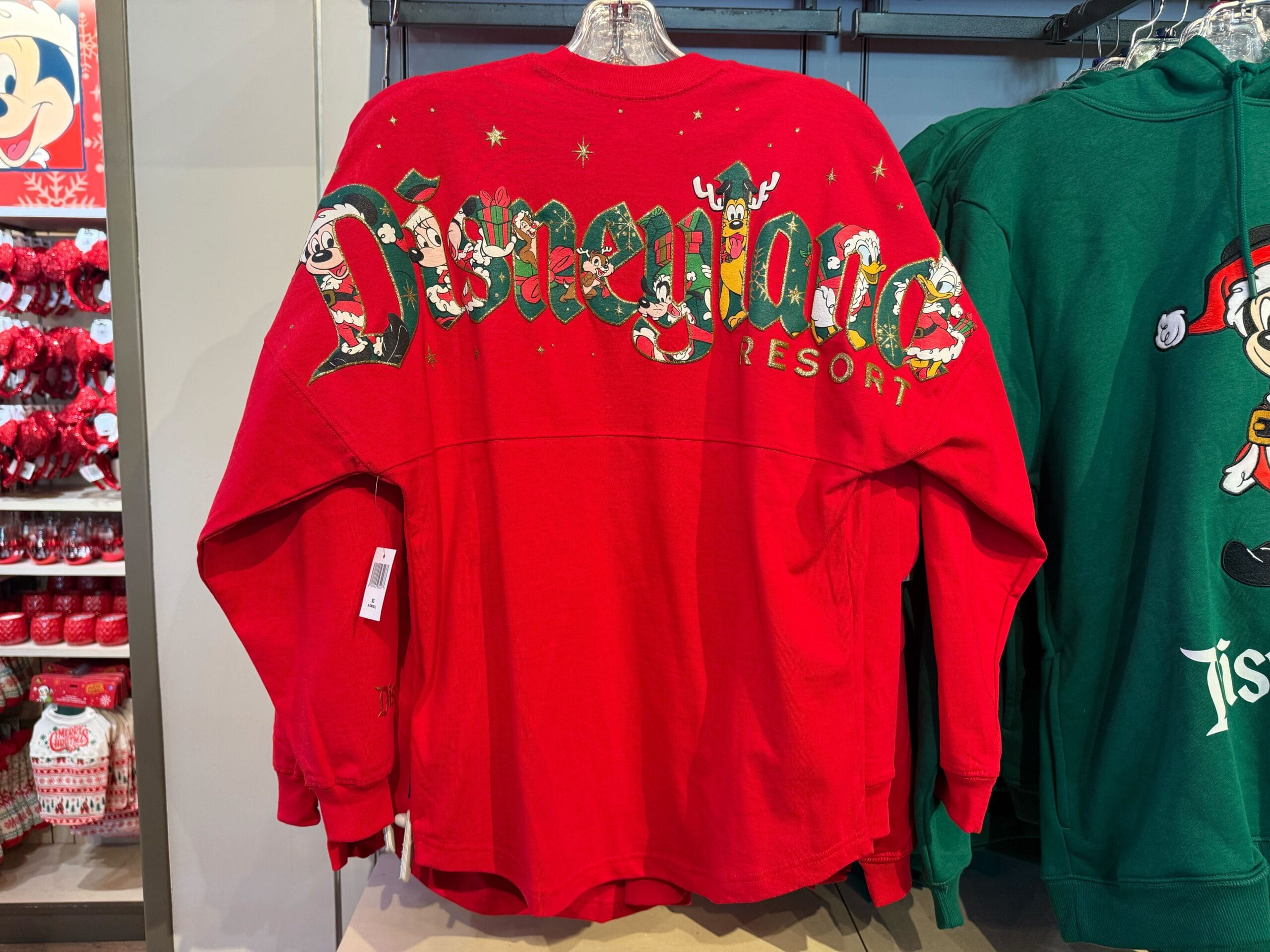 Red Disneyland Resort spirit jersey from the Christmas collection displayed beside green holiday wear, both in classic Disney Parks style.