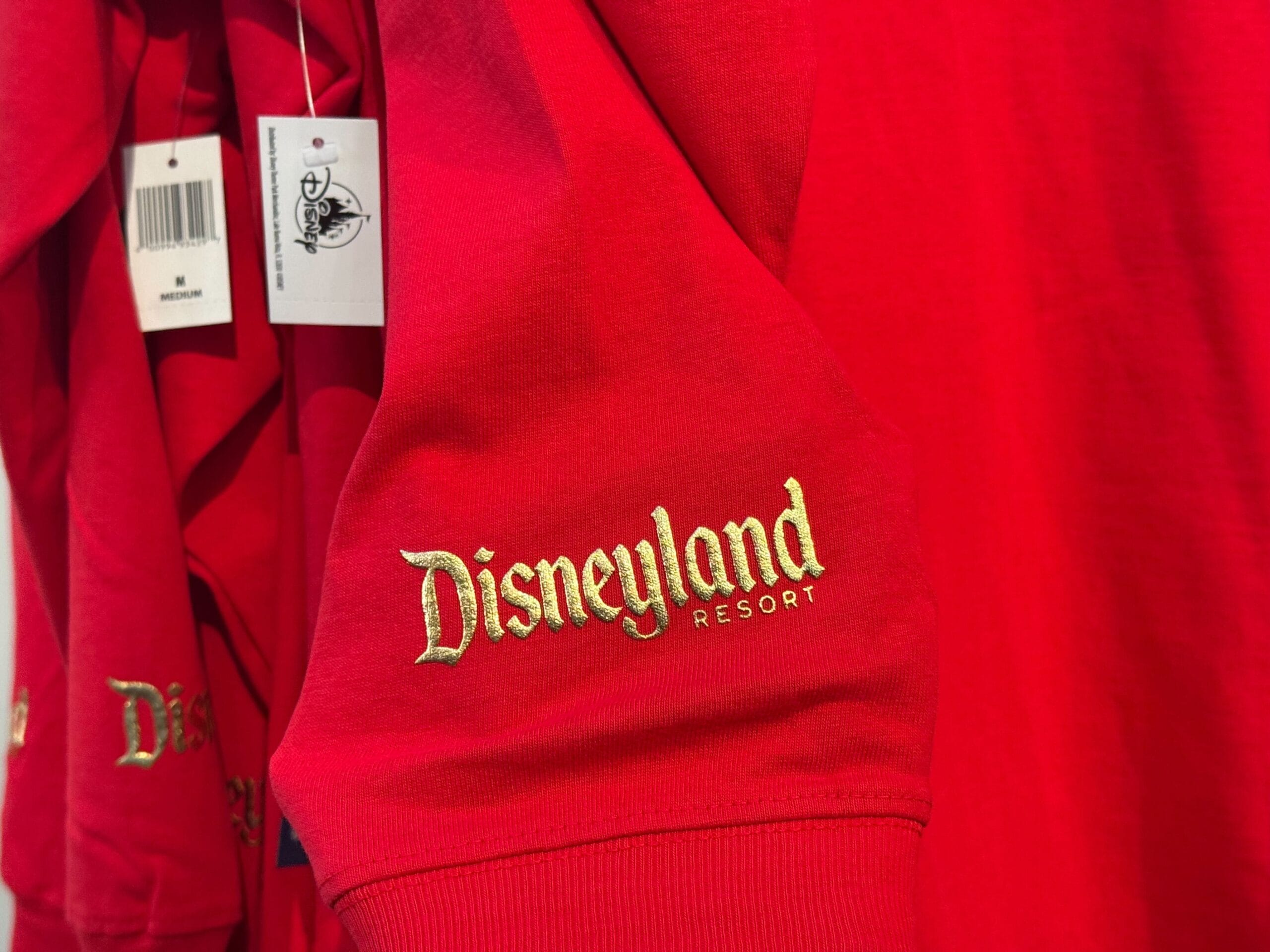 Red shirt sleeve from Disneyland Christmas merchandise, gold "Disneyland Resort" embroidery, classic style nodding to park icons.