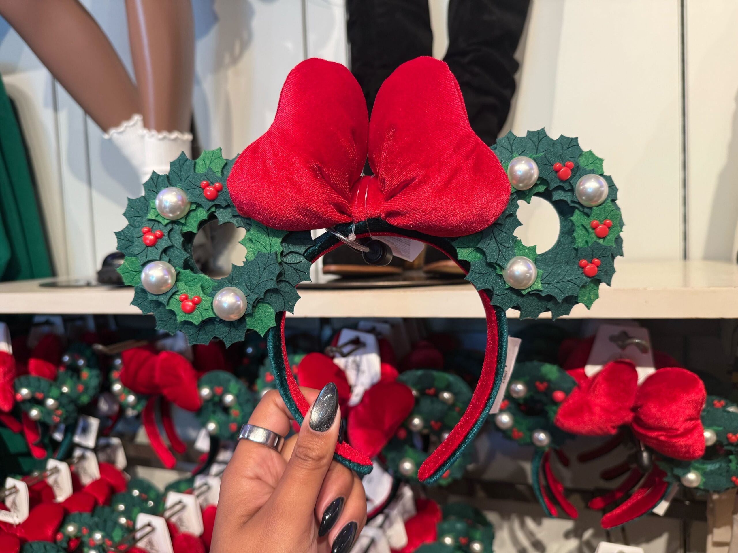 A hand holds Christmas Mickey ears from Disneyland, decorated with holly, pearls, and a velvet bow—park-exclusive holiday merch.