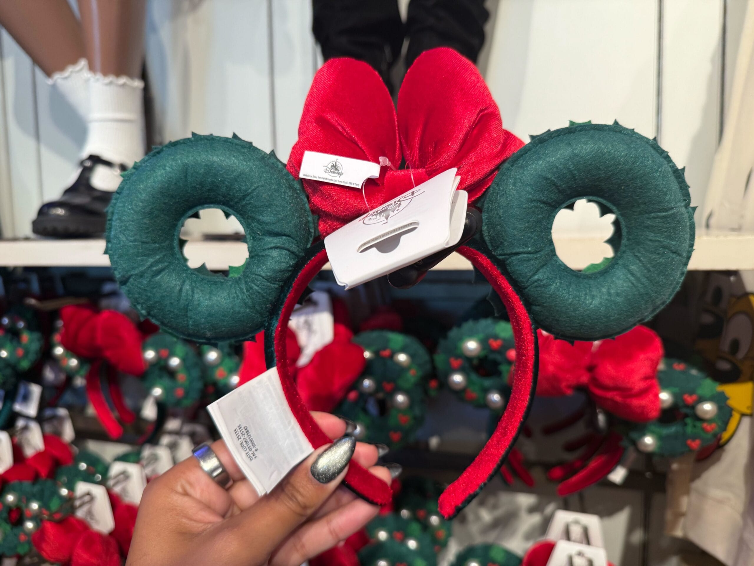 Hand holding a holiday-themed Mickey Mouse ear headband from the Peppermint Collection in a Disney park shop, not near a castle.