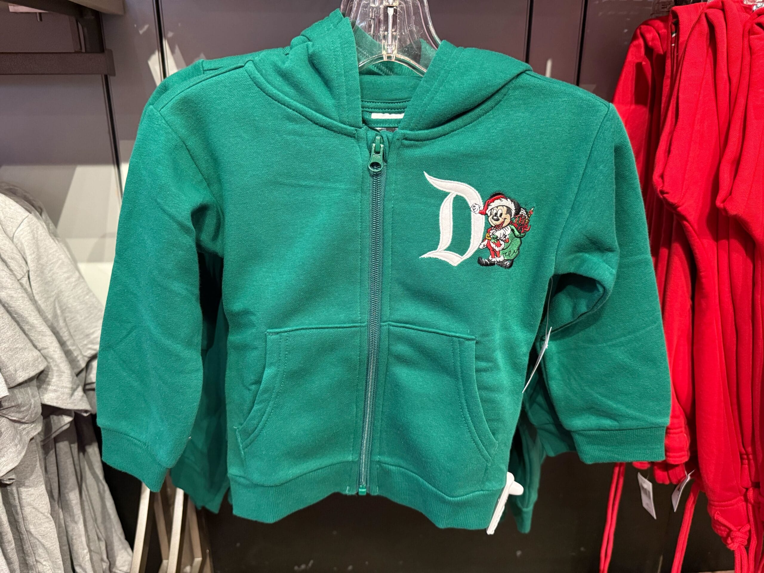 Green toddler hoodie featuring a Disney-style "D" and cartoon character, inspired by Magic Key merch, hanging on a clear hanger.