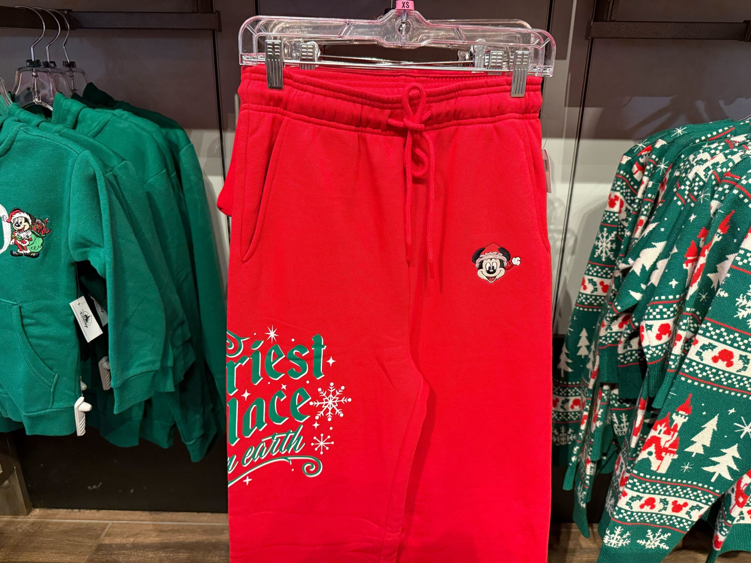 Red sweatpants with Santa-hat Mickey Mouse face, featured in a Disneyland holiday display—no castle, but classic park style.