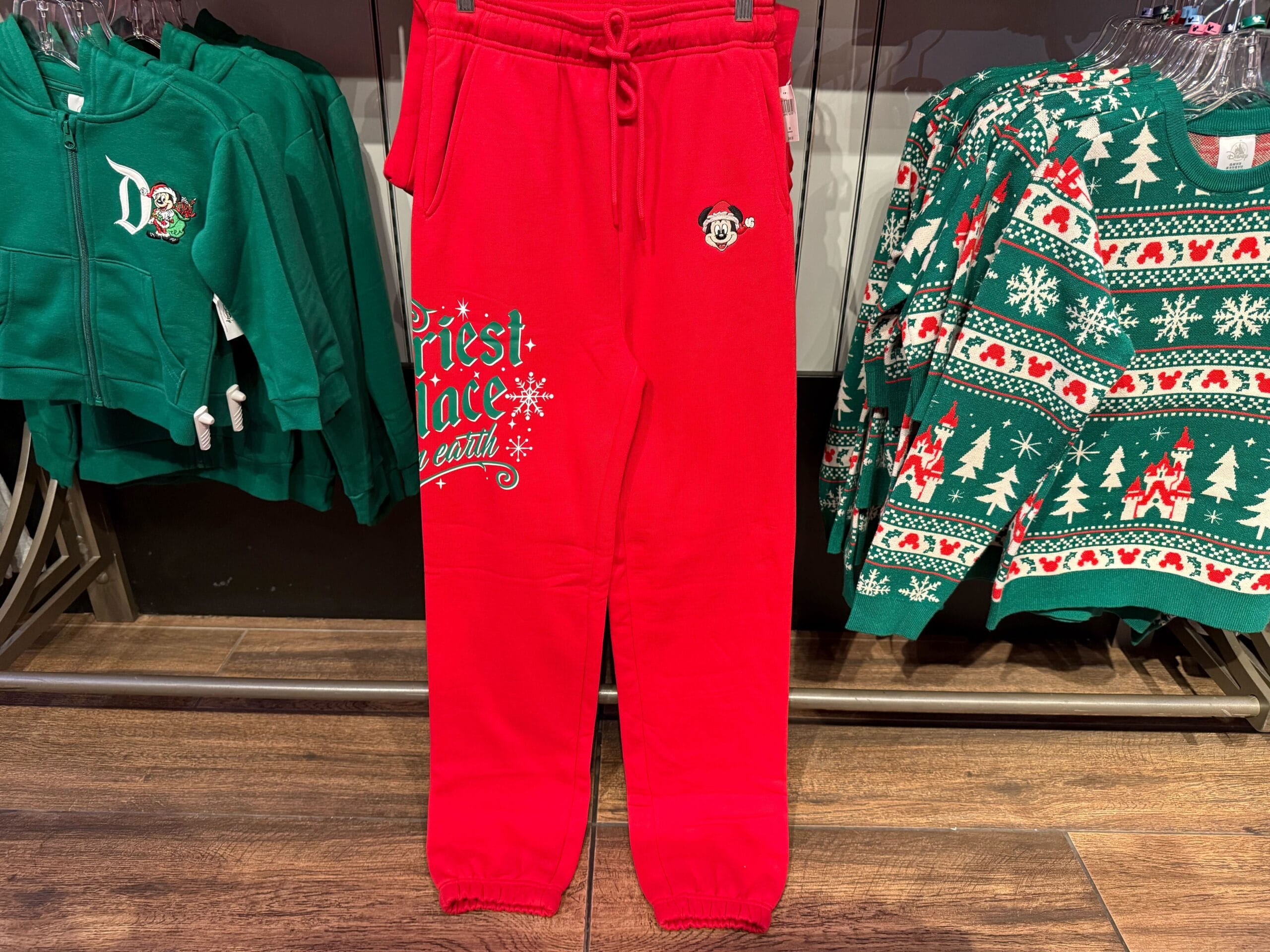 Peppermint Collection red sweatpants with festive lettering, hanging with green sweaters—like colorful Disney merch in park shops.