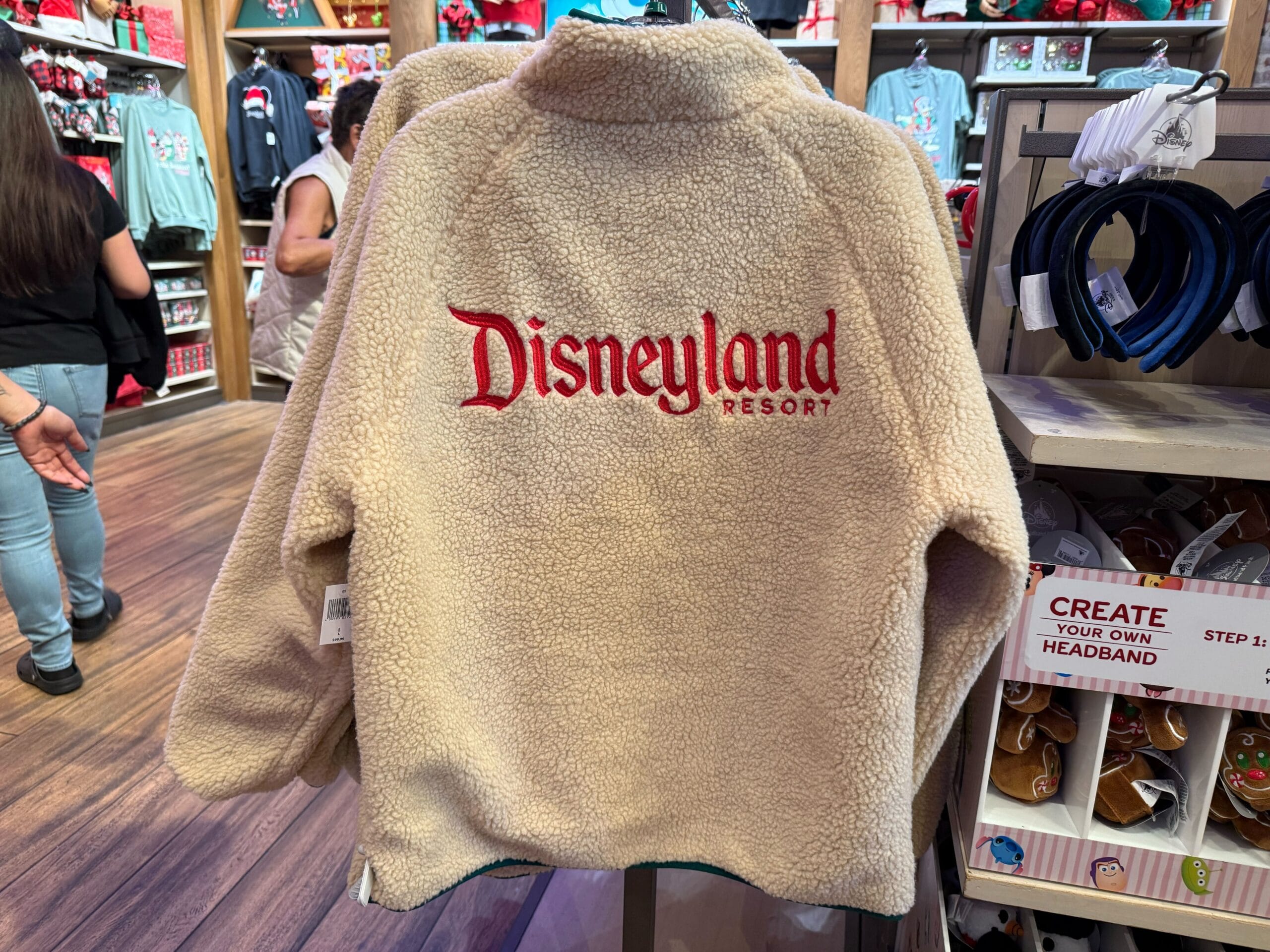 Cream fleece Disneyland Christmas jacket on display, “Disneyland Resort” in bold red on the back; exclusive park merchandise.