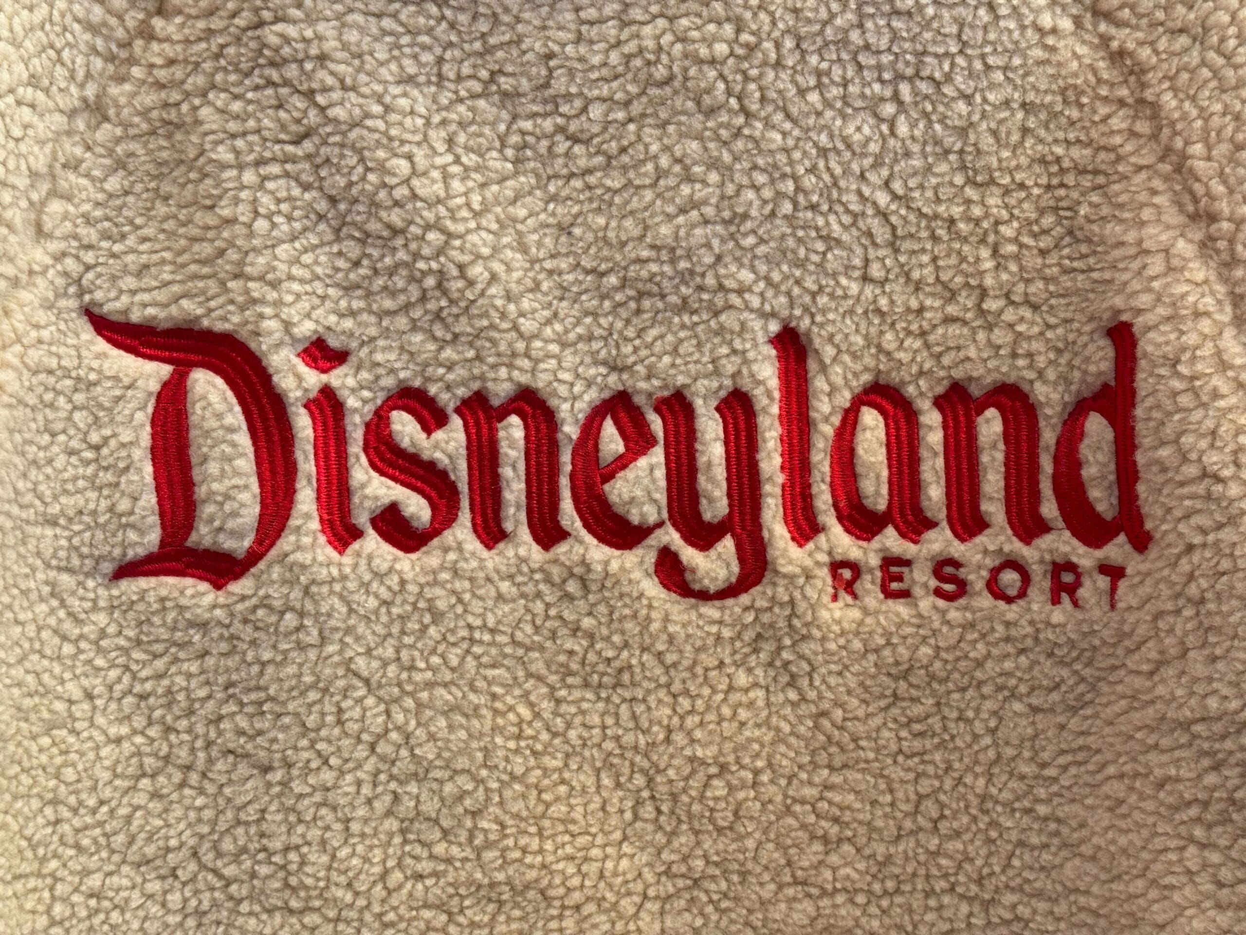 Red Disneyland Resort logo on beige sherpa Magic Key sweatshirt—evoking cozy park winters, no castle design visible.