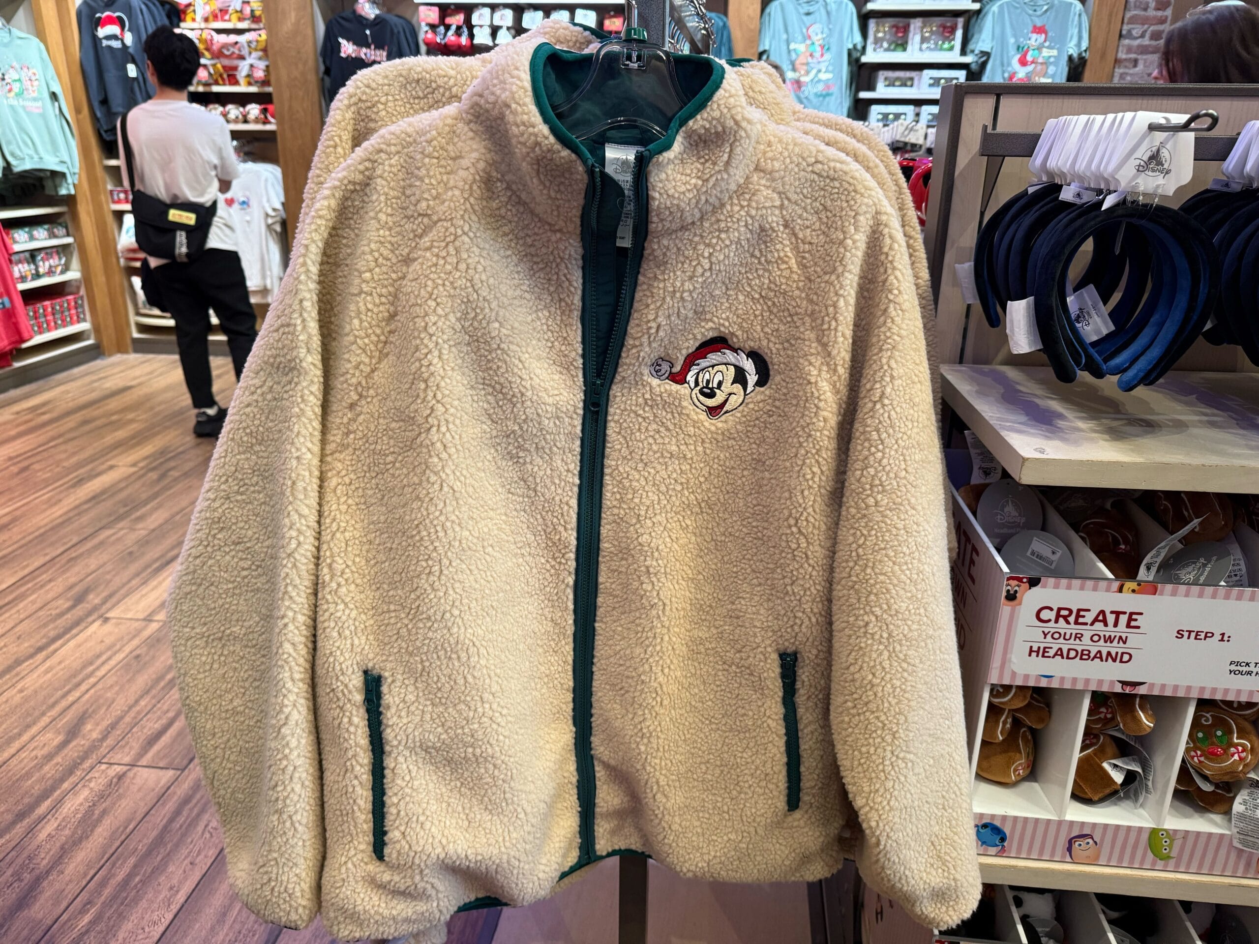 Beige fleece jacket with green zipper from the Peppermint Collection, featuring festive Mickey Mouse embroidery seen at Disney Parks.