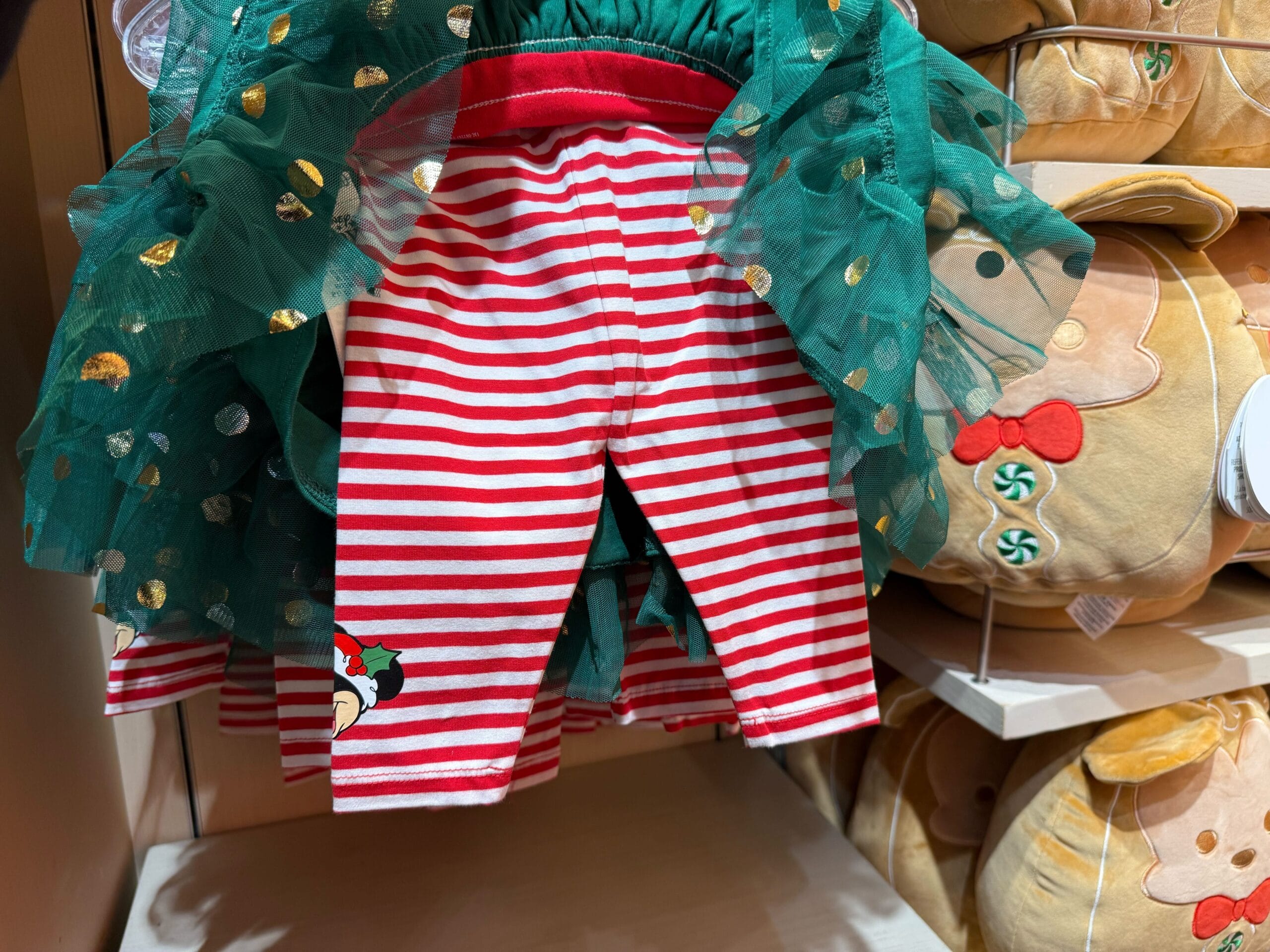 Red and white striped children’s leggings with a green tutu from the Peppermint Collection, displayed by gingerbread plush toys, as seen in Disney Parks holiday shops.