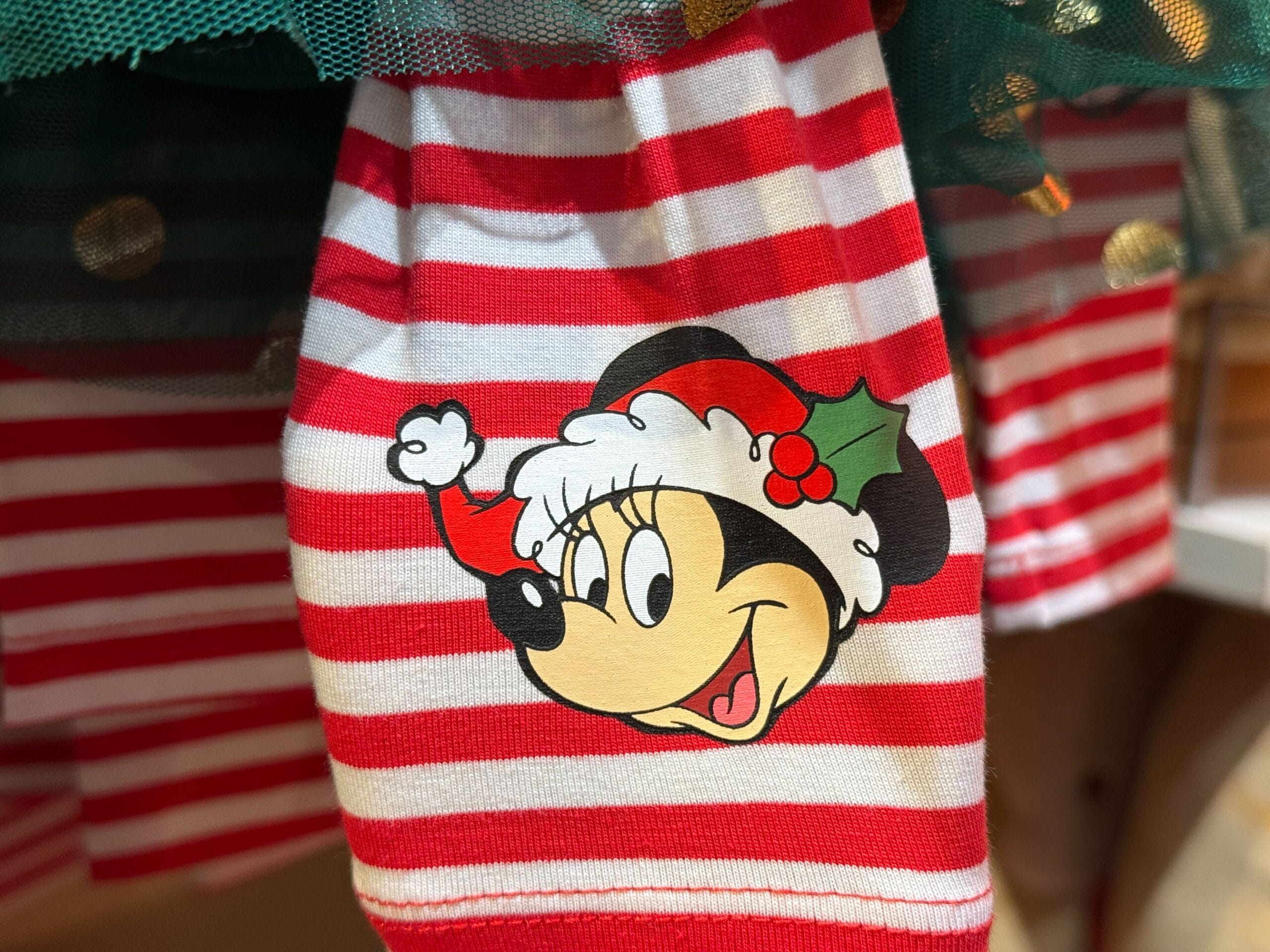 Close-up of Minnie Mouse in a Santa hat on red and white striped Peppermint Collection fabric, festive Disney Park style.