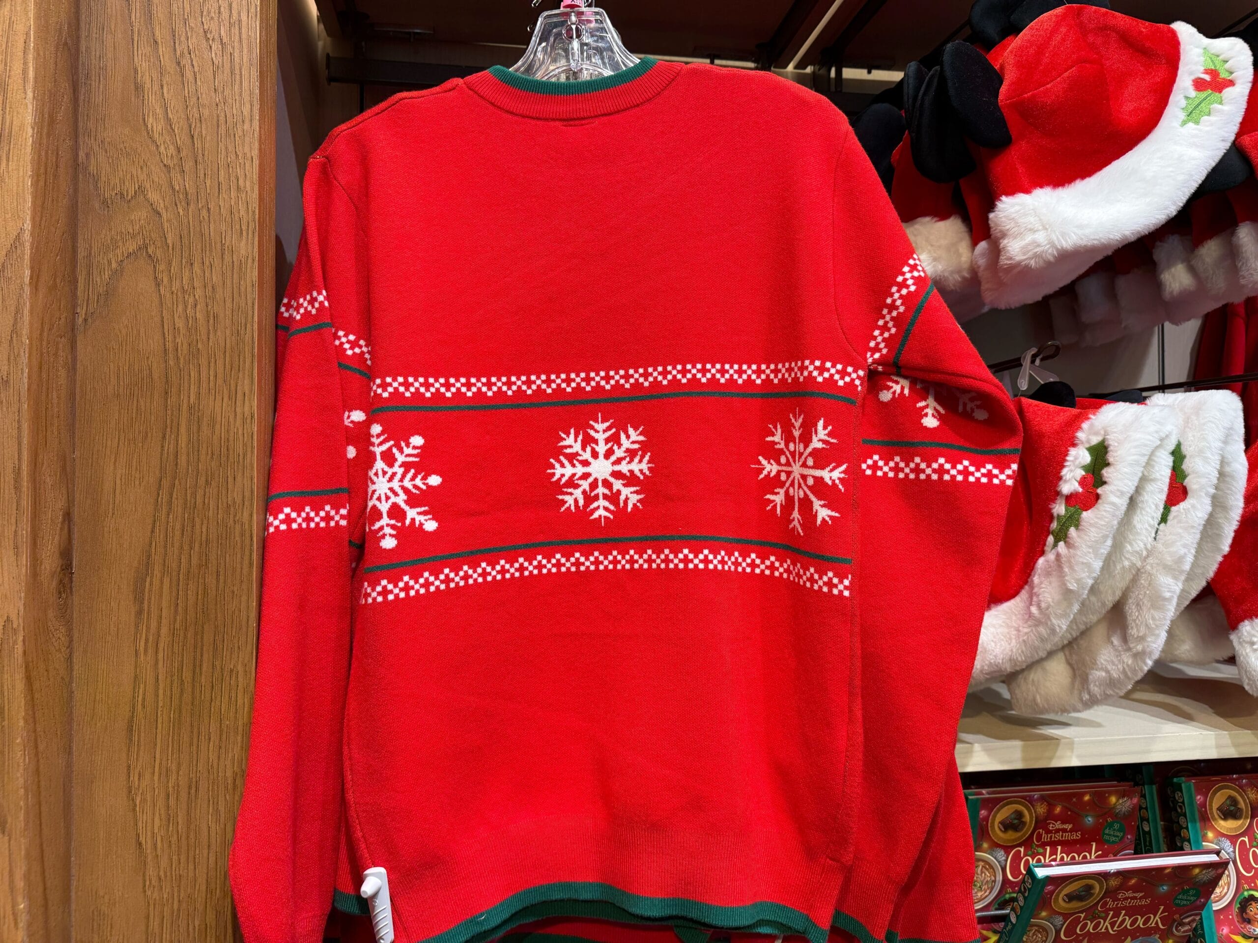 A red sweater with white snowflakes hangs among Disneyland holiday items, with festive decor evoking Main Street, U.S.A.'s cozy charm.