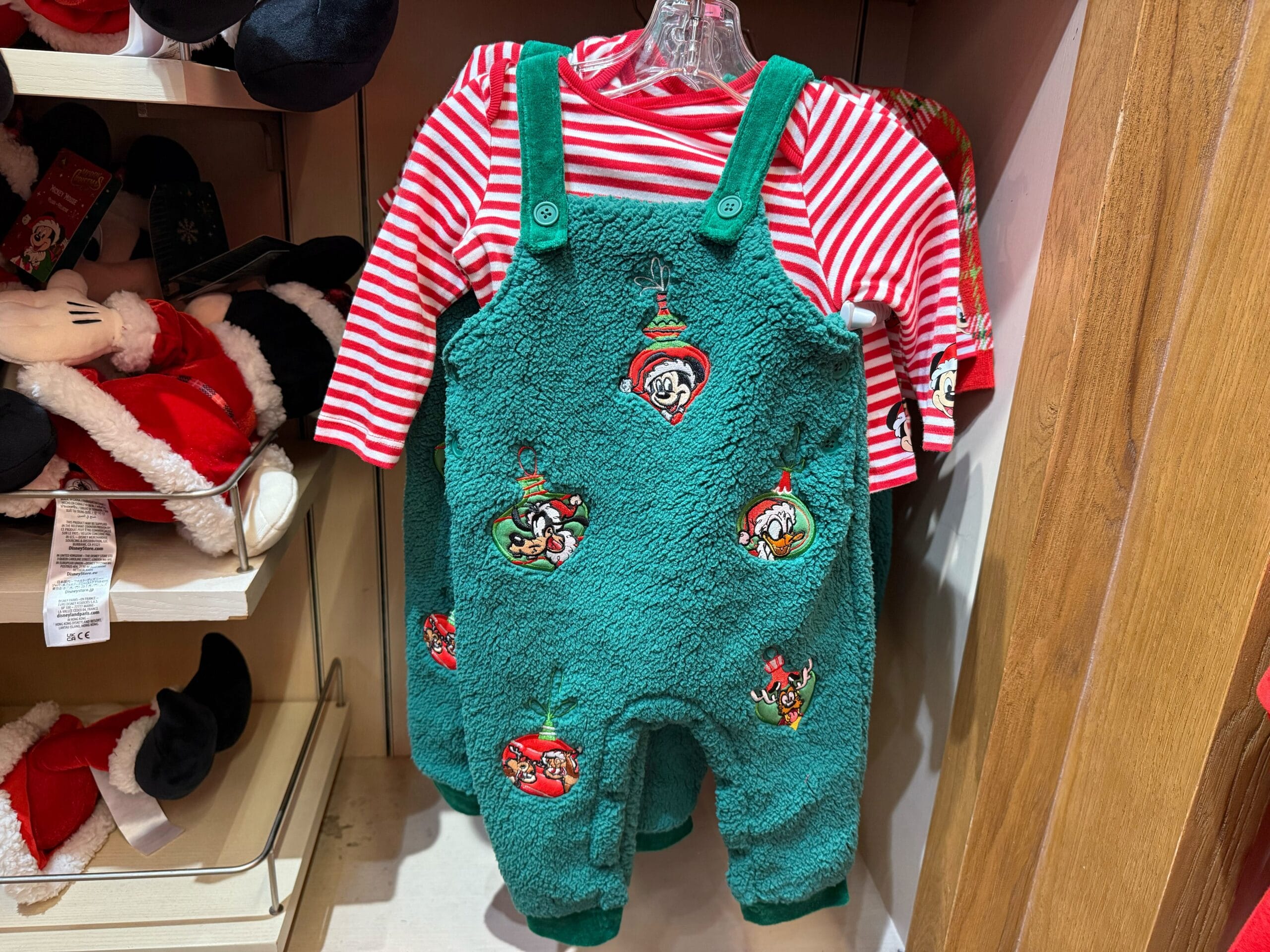 Green fuzzy baby overalls with cartoon accents from the Peppermint Collection, over a red-and-white striped shirt; classic Disney style.