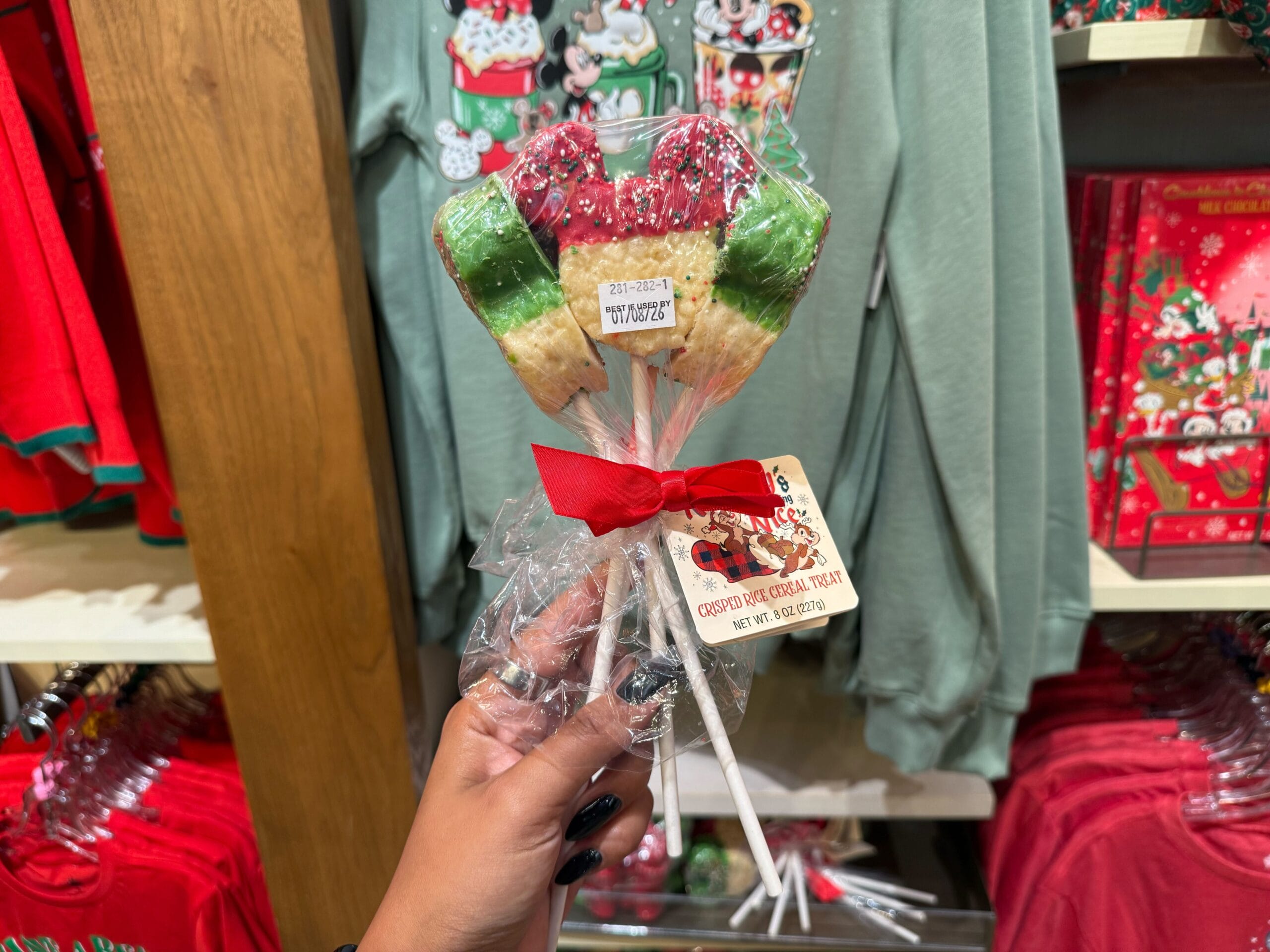 Hand holding festive crispy rice treats on sticks from Disneyland’s Peppermint Collection, exclusive to the park’s holiday lineup.