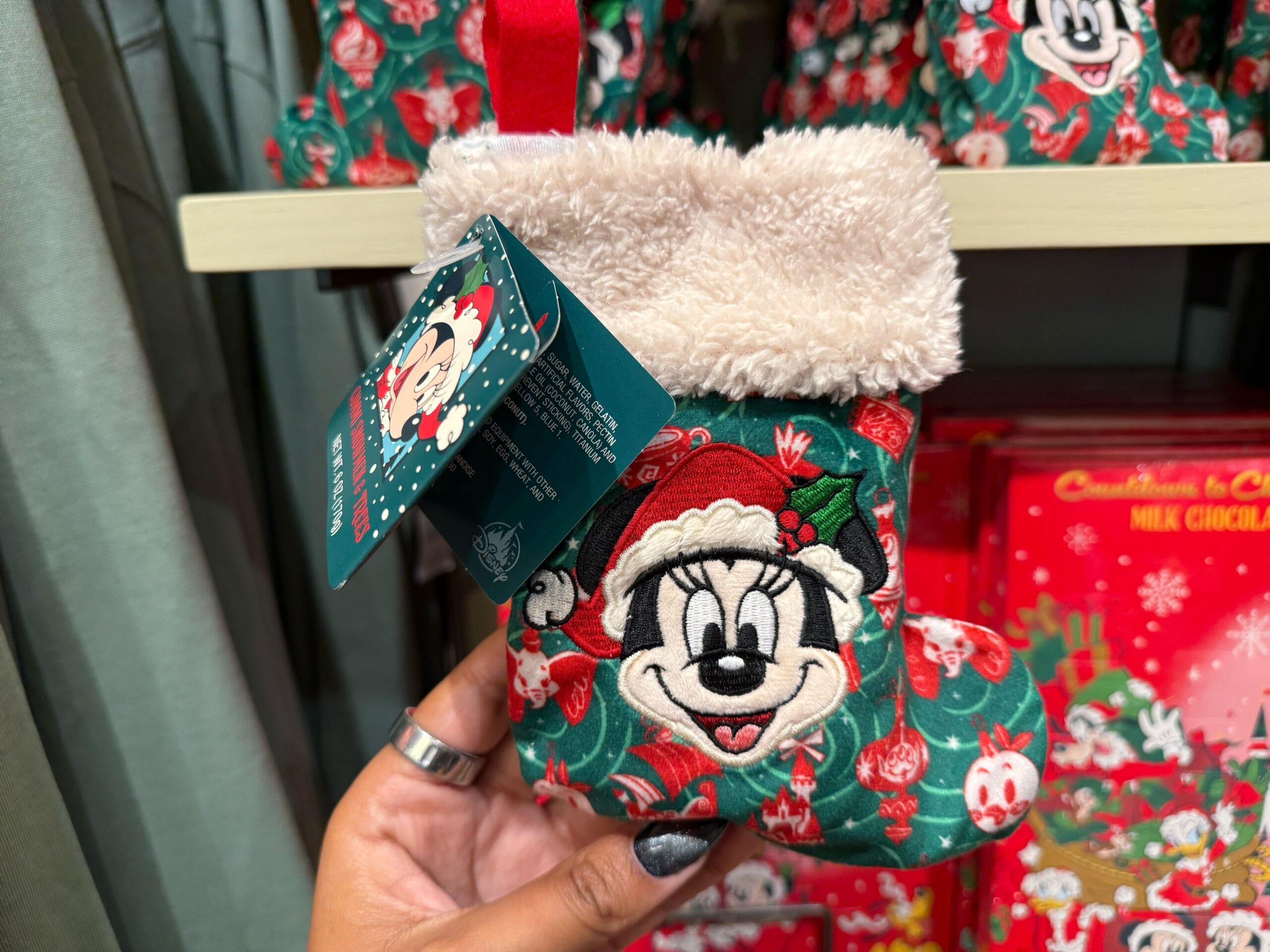 A hand holds a small Minnie Mouse Christmas stocking from Disneyland; no castle pictured, but similar stockings sold at Disney parks worldwide.