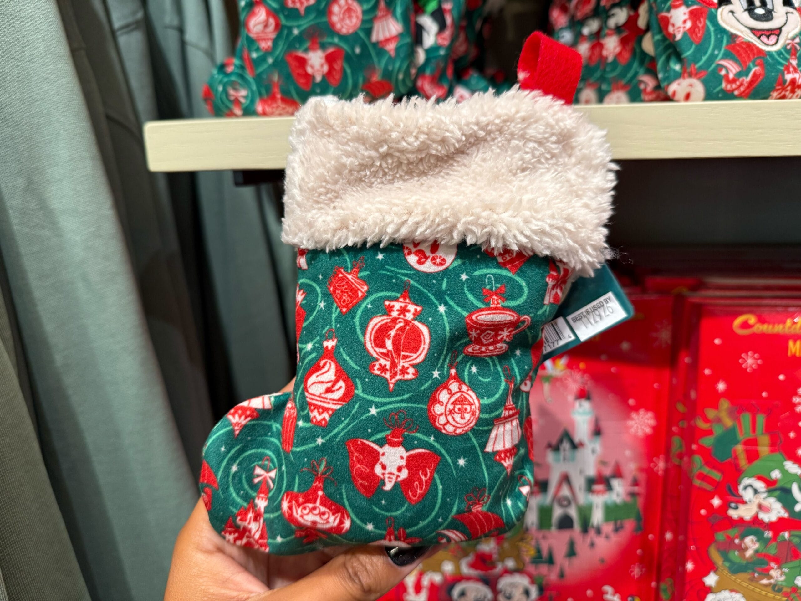 A hand holds a small green and red Christmas stocking from the Peppermint Collection, with festive patterns like in Disney Parks shops.