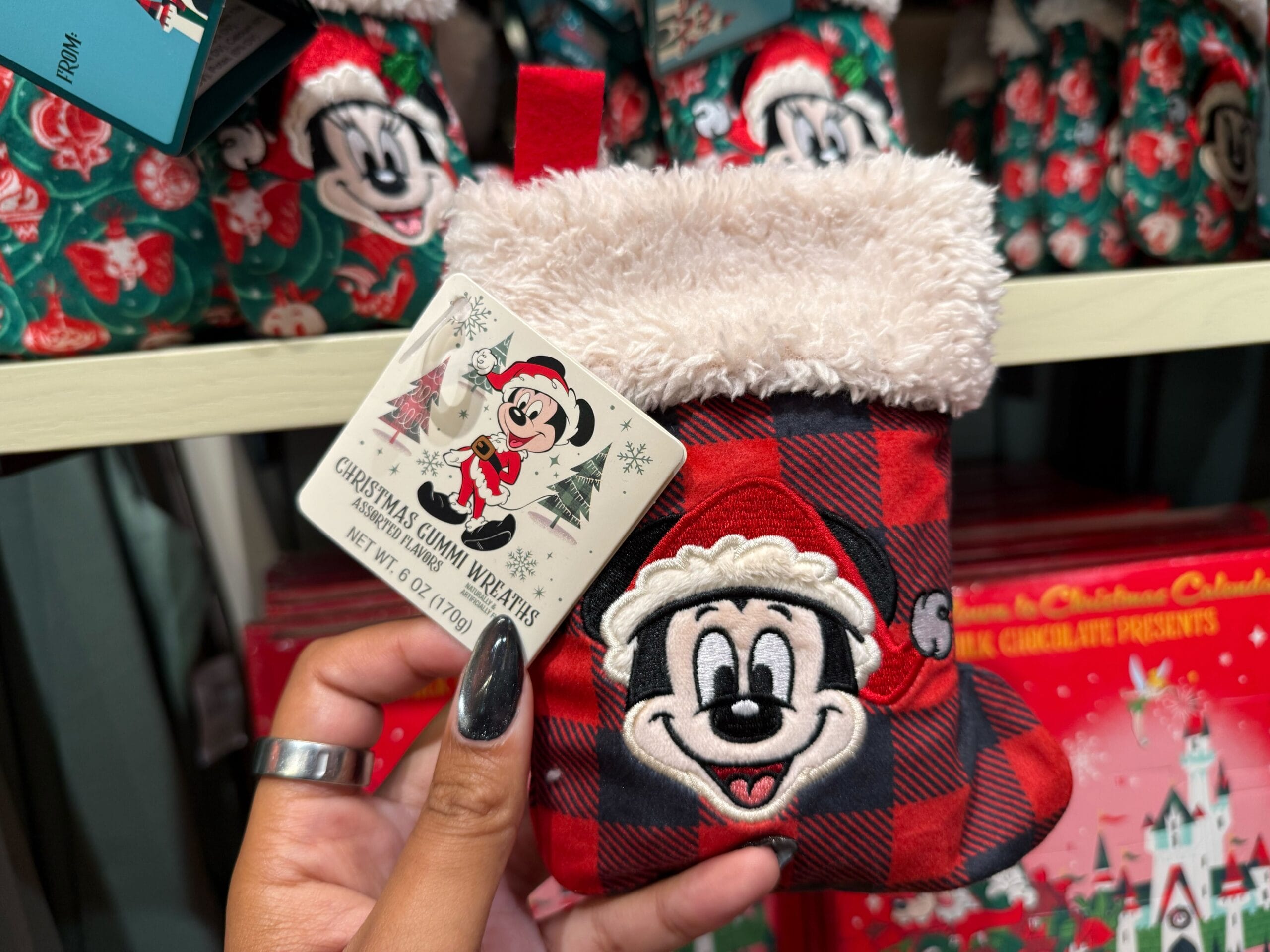 A hand displays a small red plaid Christmas stocking with Mickey from Disneyland’s holiday merchandise, reminiscent of park souvenirs.