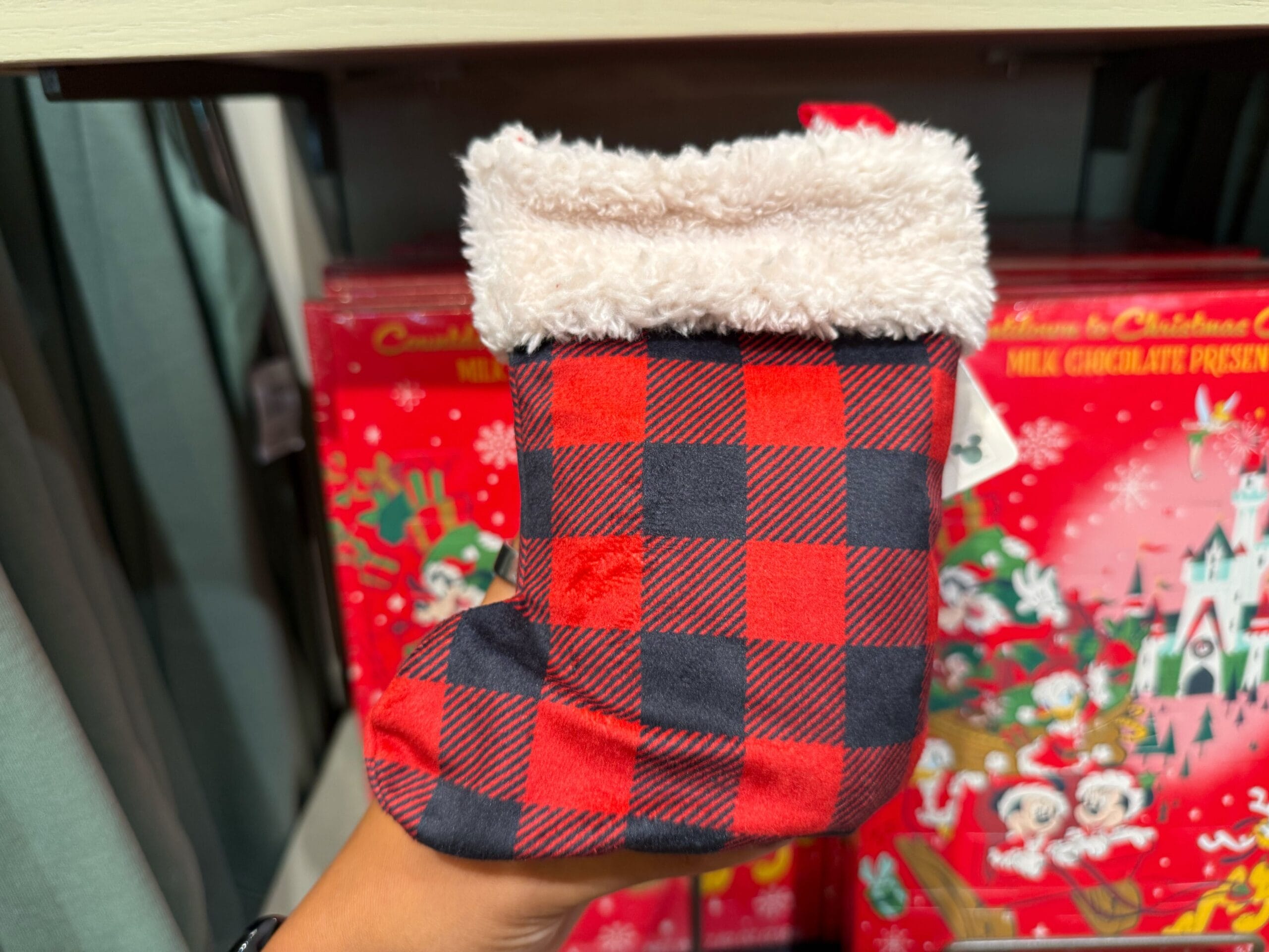 A hand holds a small red and black plaid Christmas stocking from Disneyland’s holiday collection, evoking festive park spirit.