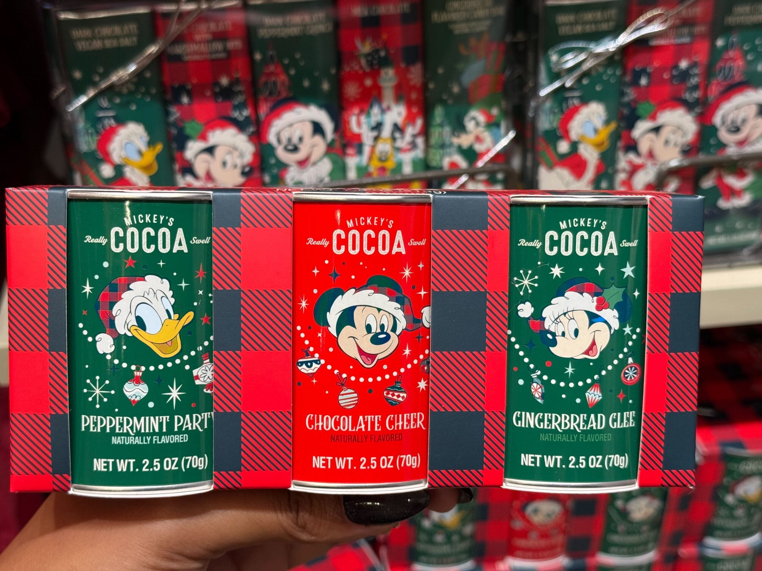 Three tins of Mickey’s Cocoa—Donald, Mickey, and Minnie in festive holiday designs—evoking park treat vibes from Disney resorts.