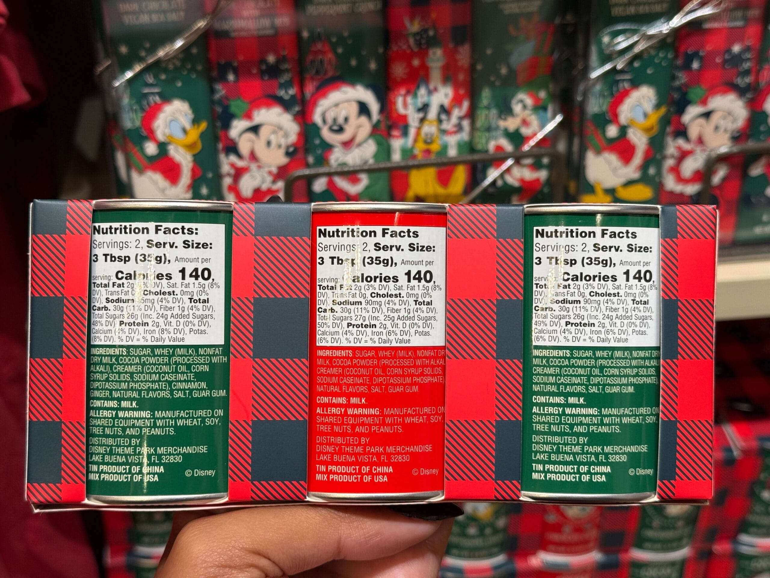 Three Disneyland holiday food packages with nutrition labels, held in hand, featuring festive designs from the park’s Christmas collection.