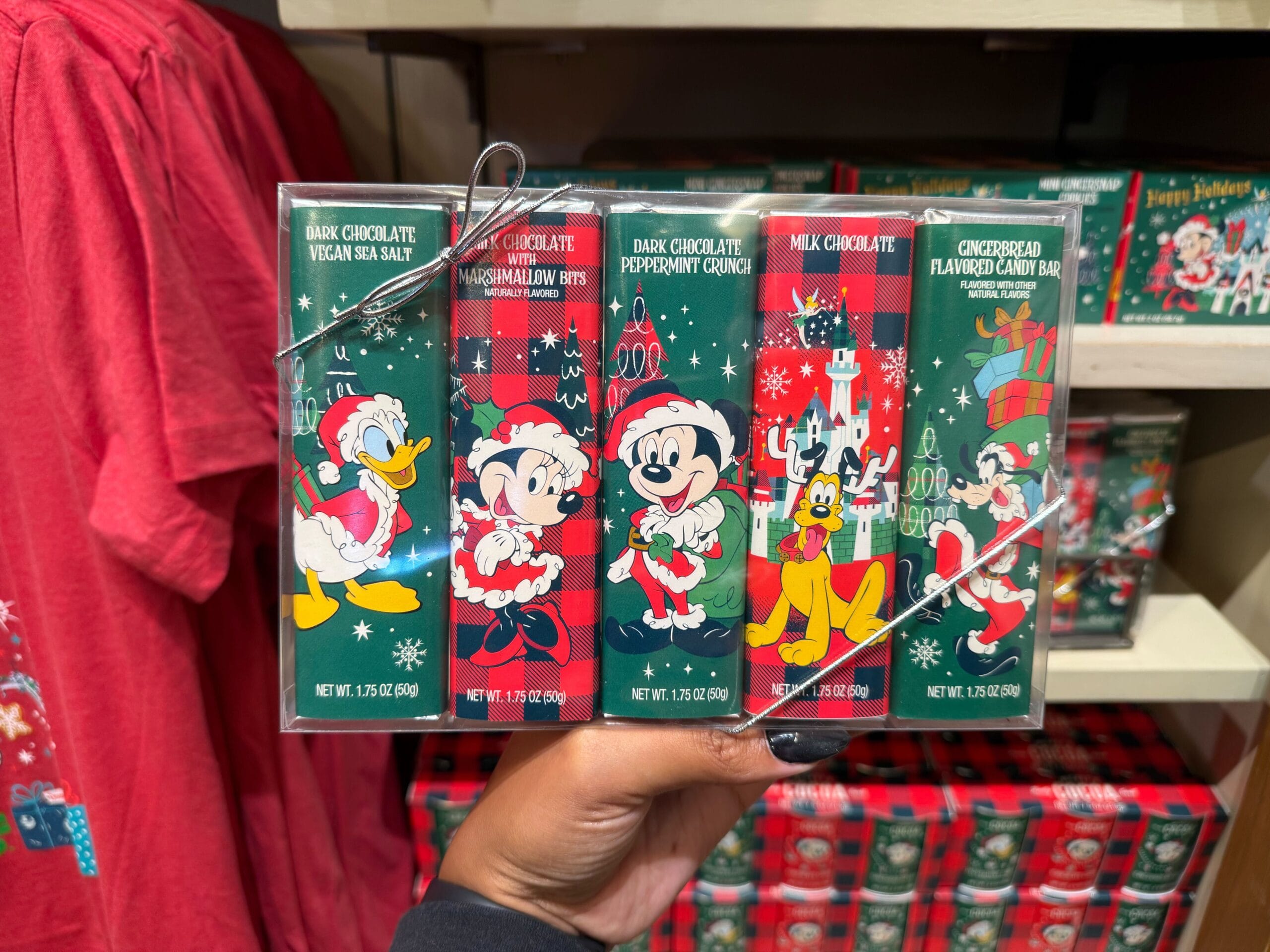 Hand holding Christmas-themed chocolate bars with Disney characters in festive outfits, exclusive to Disneyland park merchandise.
