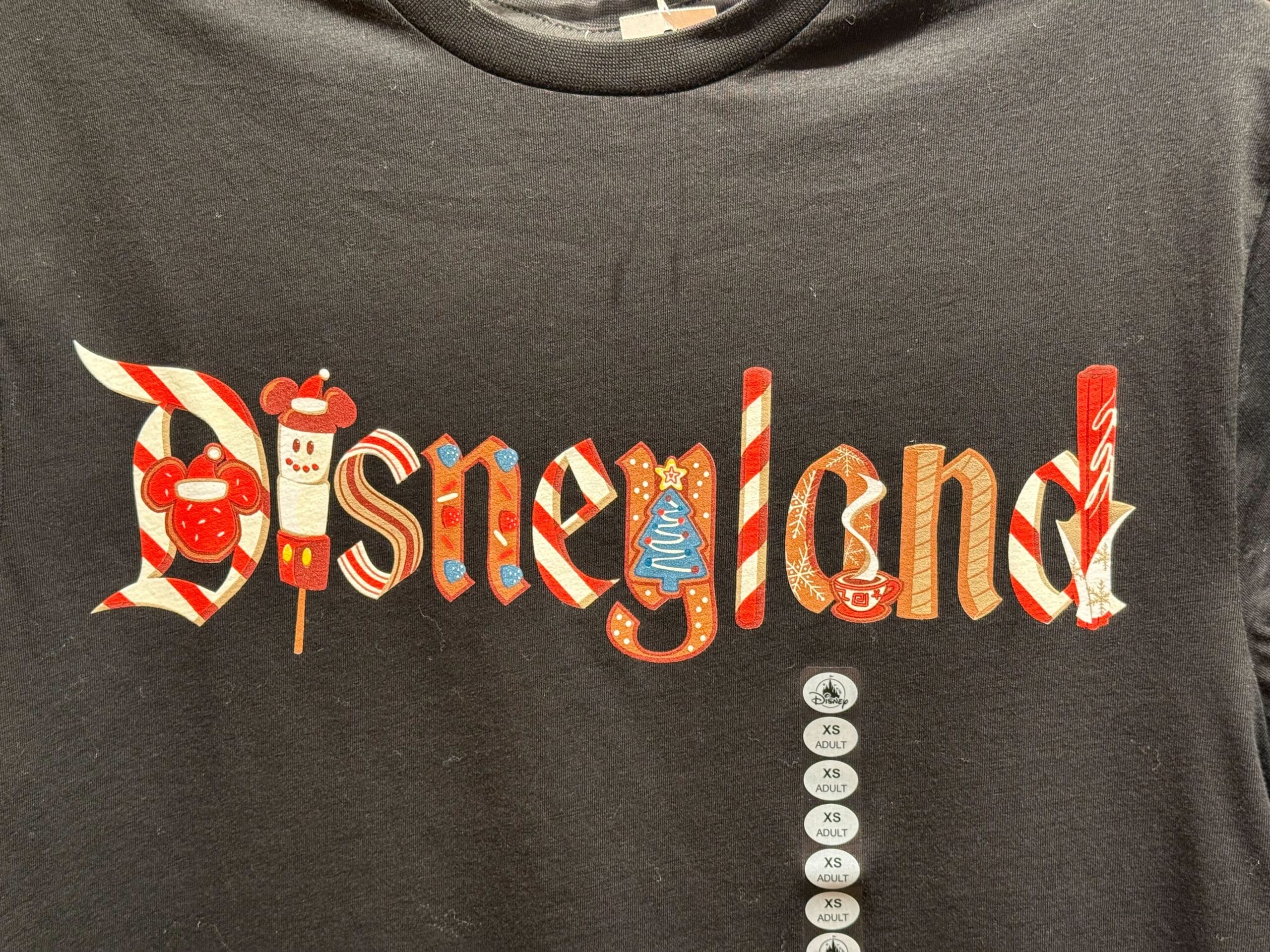 Black shirt with "Disneyland" spelled out in colorful candy-style letters, festive holiday apparel exclusive to Disneyland Resort.