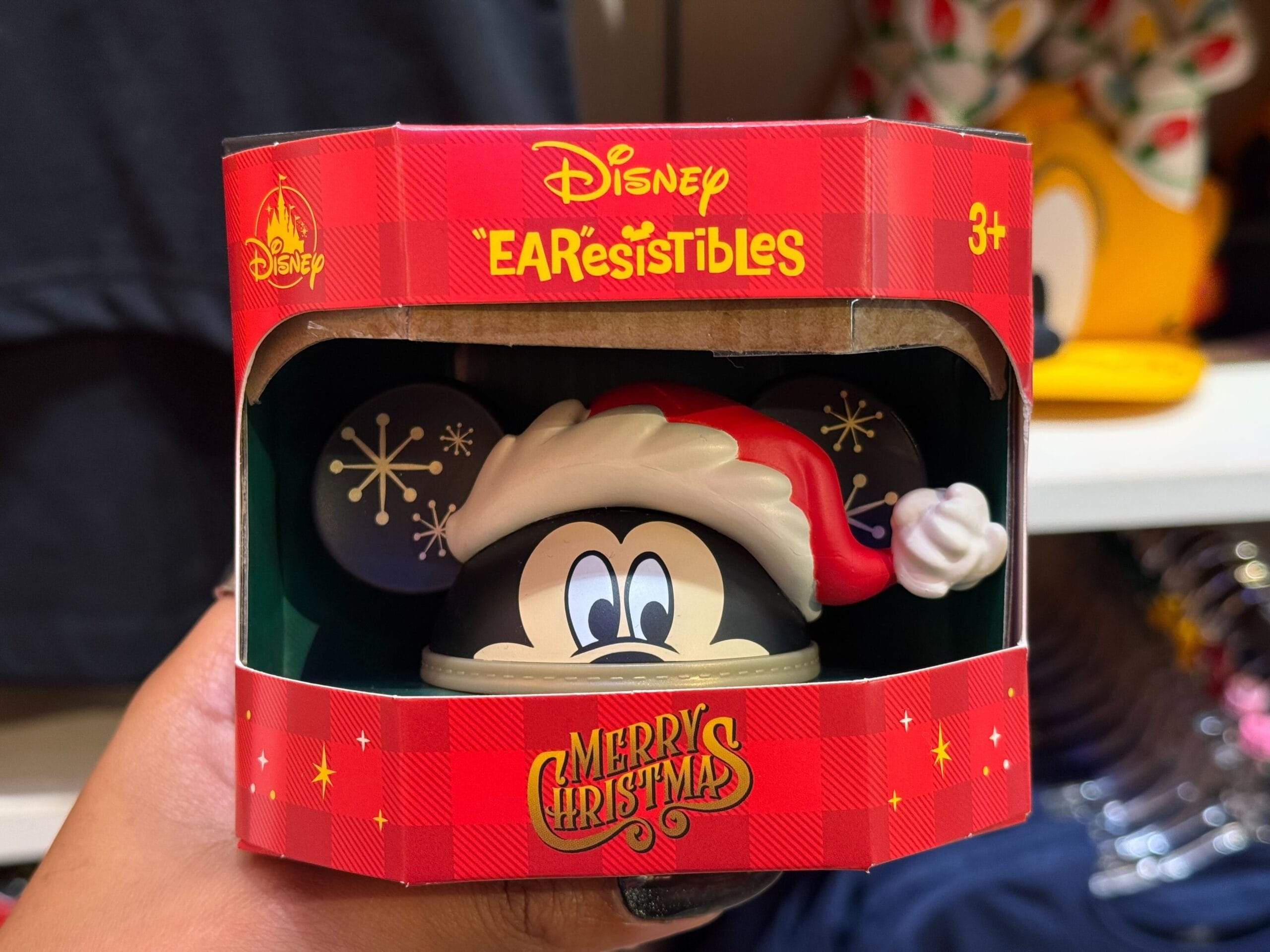 A hand displays a Disneyland Christmas “EARSistibles” Mickey ornament in festive packaging, perfect for Disney park holiday fans.