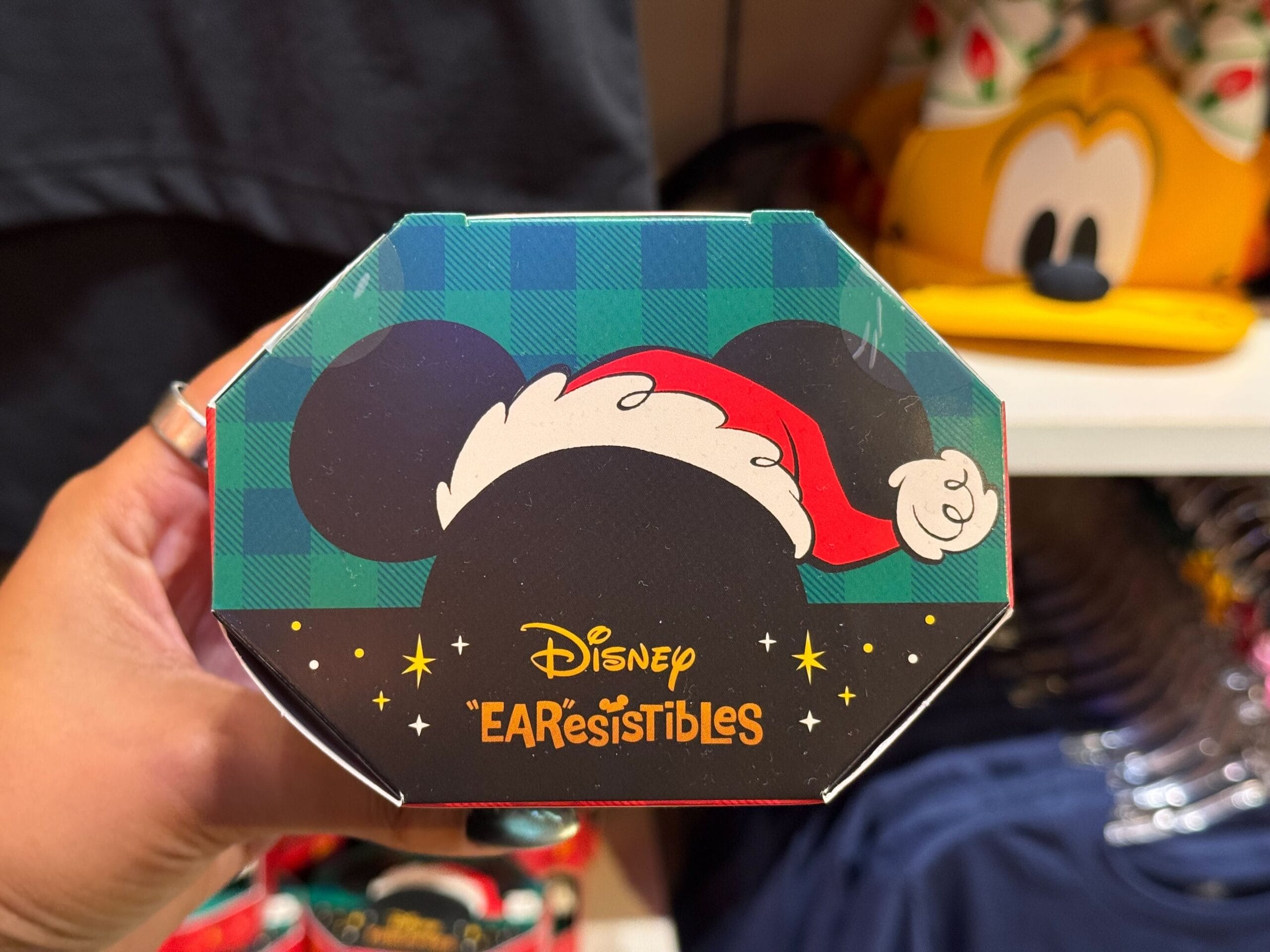 A hand holds a Disney “EARresistibles” box with Mickey ears in a Santa hat, part of Disneyland’s holiday merchandise selection.