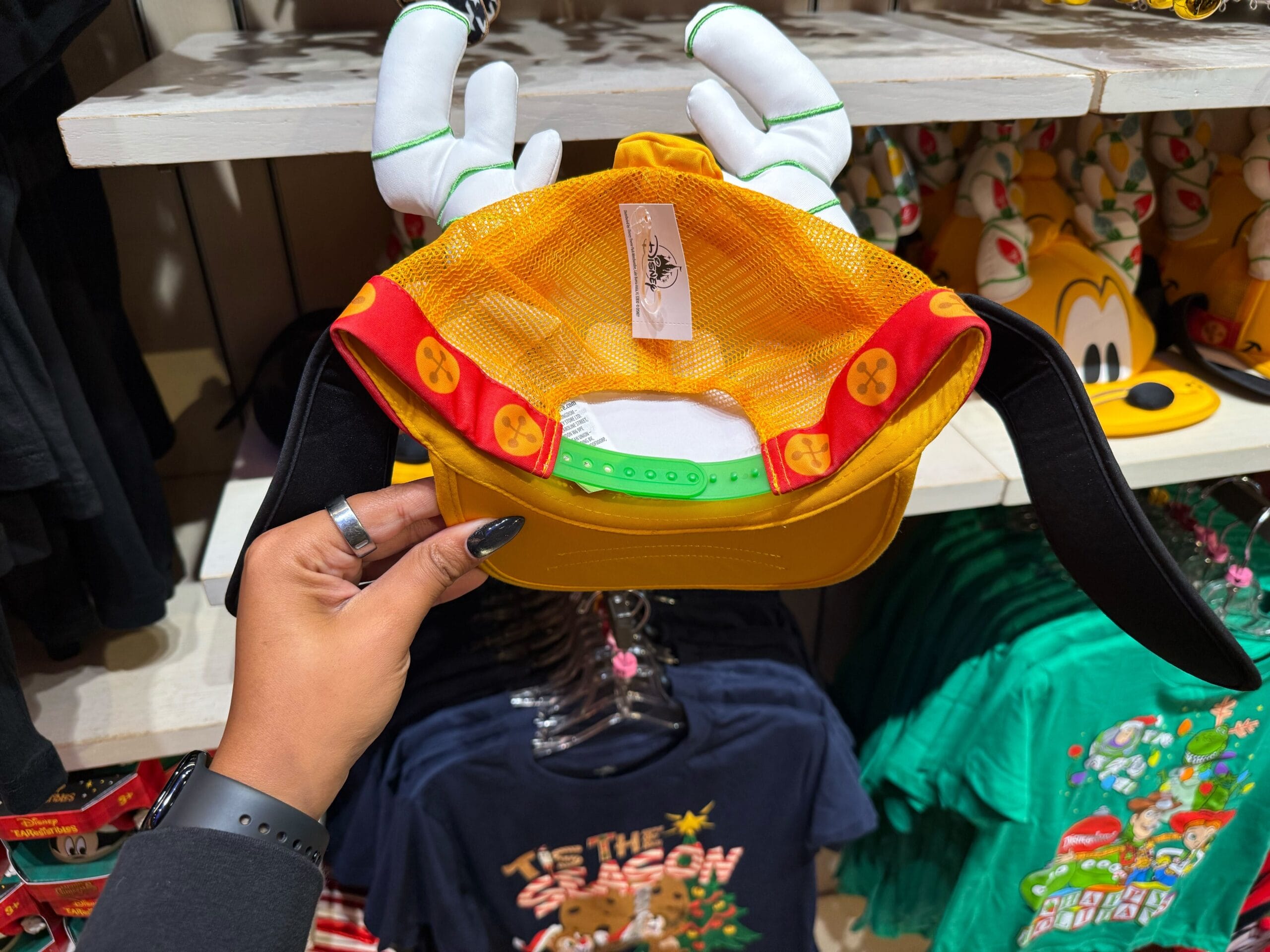 A person displays a Goofy hat with floppy ears and gloves among Disneyland holiday merchandise—no castle like Disney World's here.