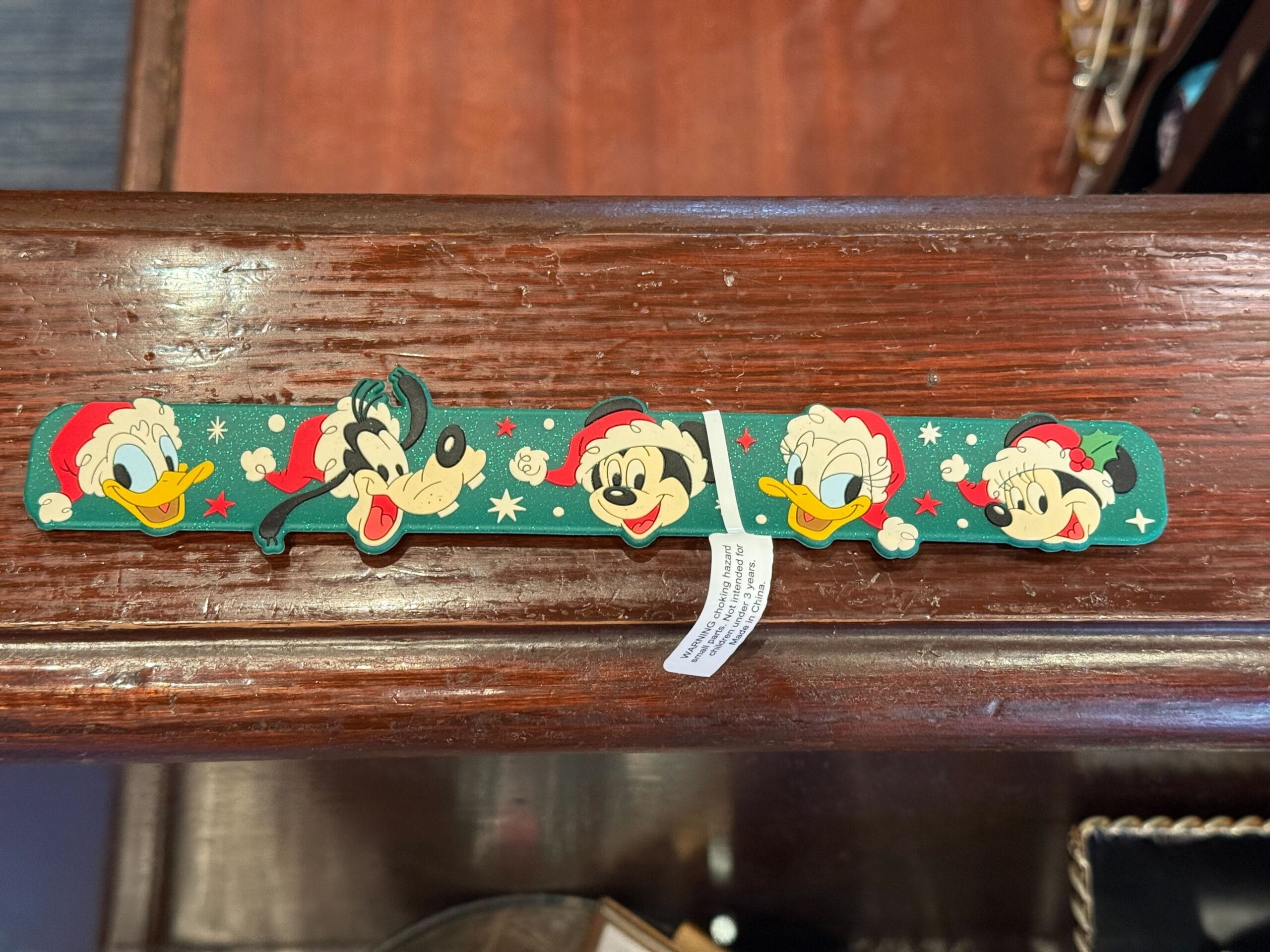 Festive green slap bracelet with Disney characters in Santa hats—holiday merch from Disneyland Resort, home to Sleeping Beauty Castle.