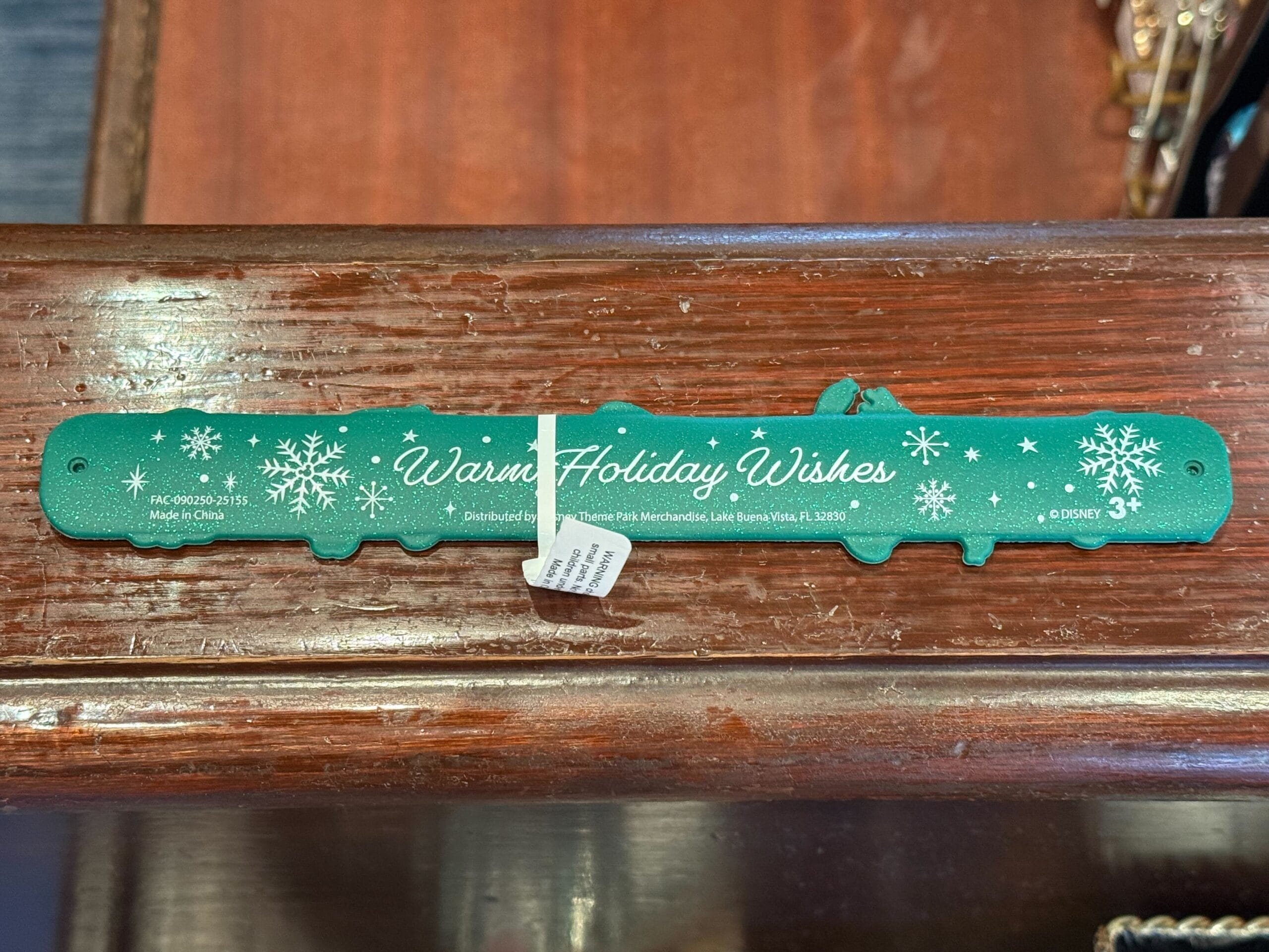 Green slap bracelet featuring white snowflakes and "Warm Holiday Wishes," exclusive to Disneyland Resort—Magic Kingdom style, not Cinderella Castle.