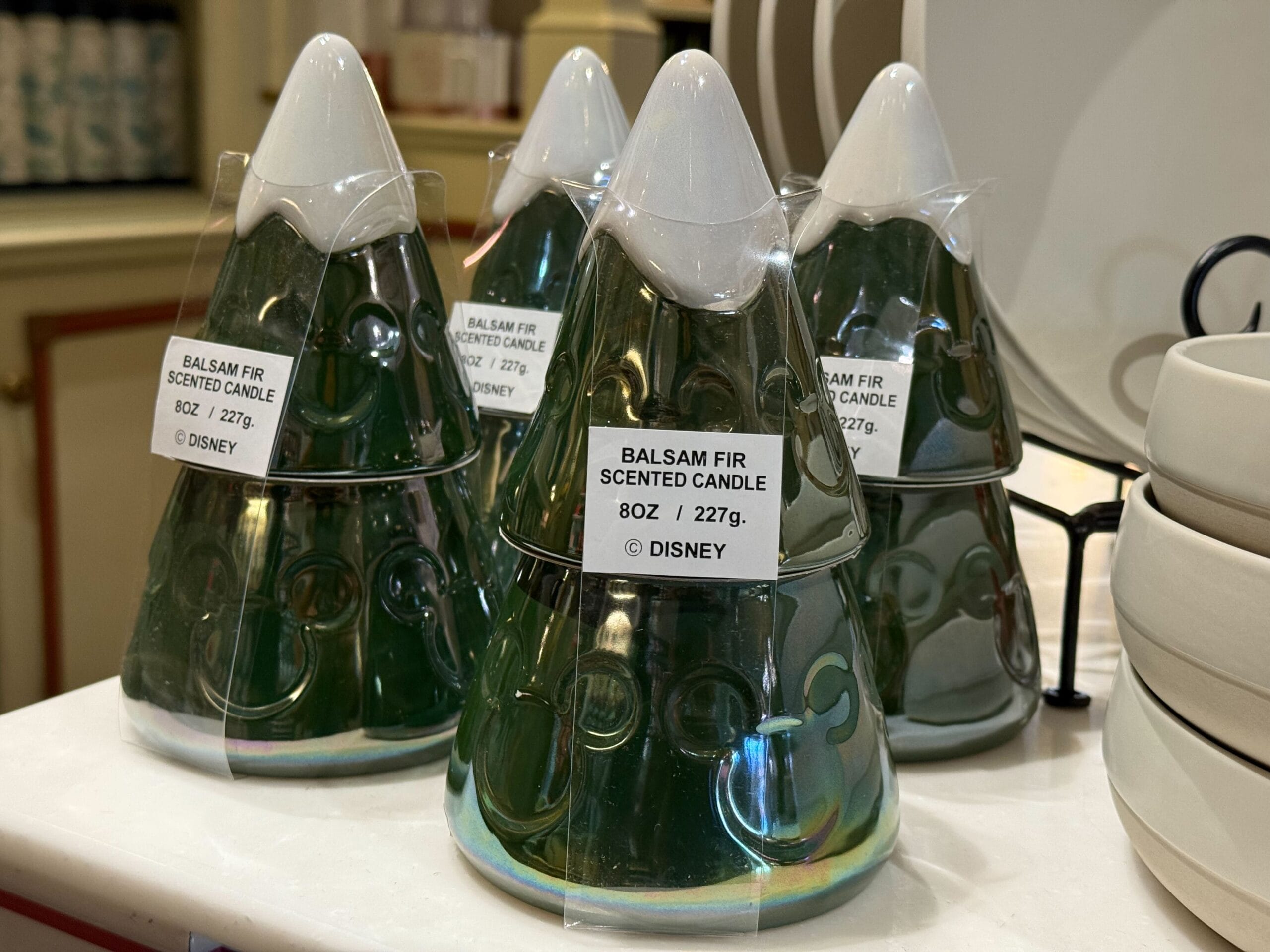Green, tree-shaped balsam fir candles line a shelf at Disneyland Resort, festive merchandise beneath Sleeping Beauty Castle's charm.