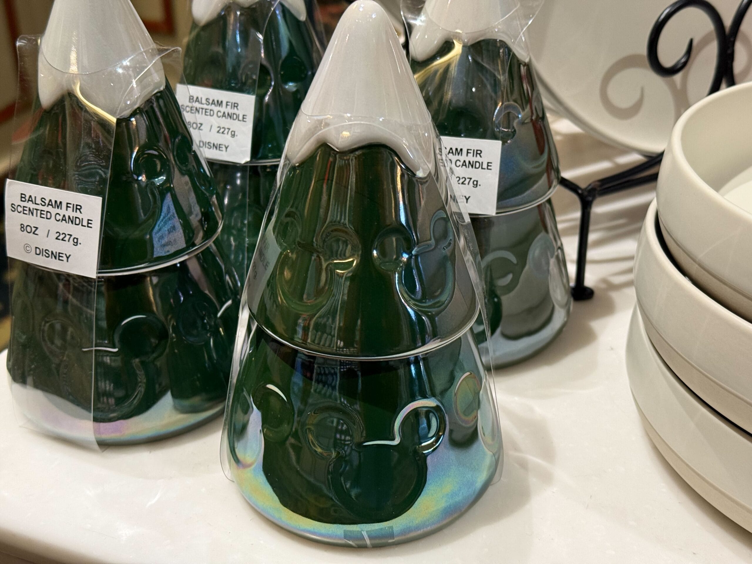 Green, tree-shaped Disney balsam fir candles with Mickey Mouse designs, new arrivals displayed by plates at a Disney Park store.