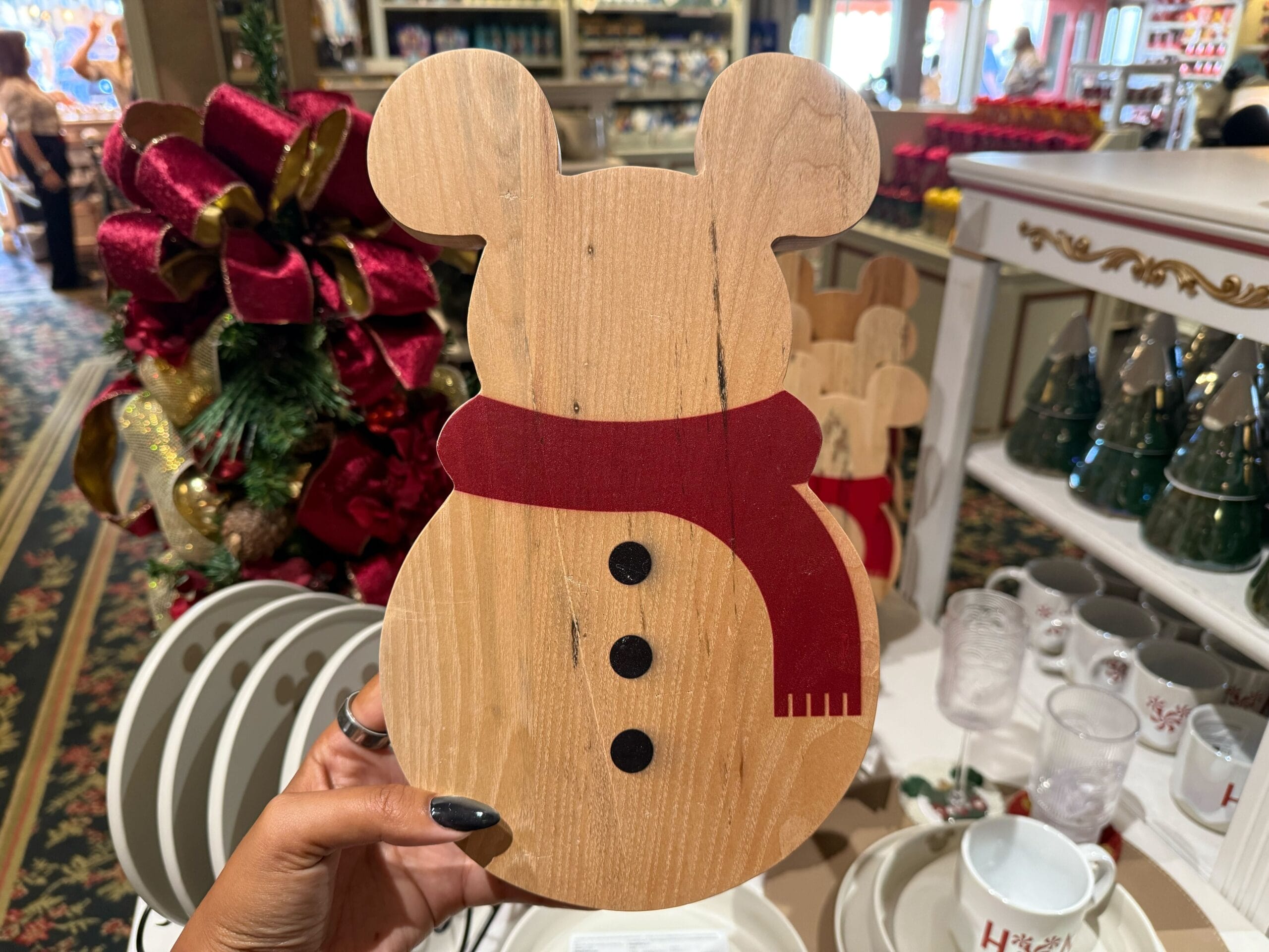 A hand holds a wooden Mickey Mouse snowman ornament, festive Disneyland Resort merchandise—no castle like those at any park in view.