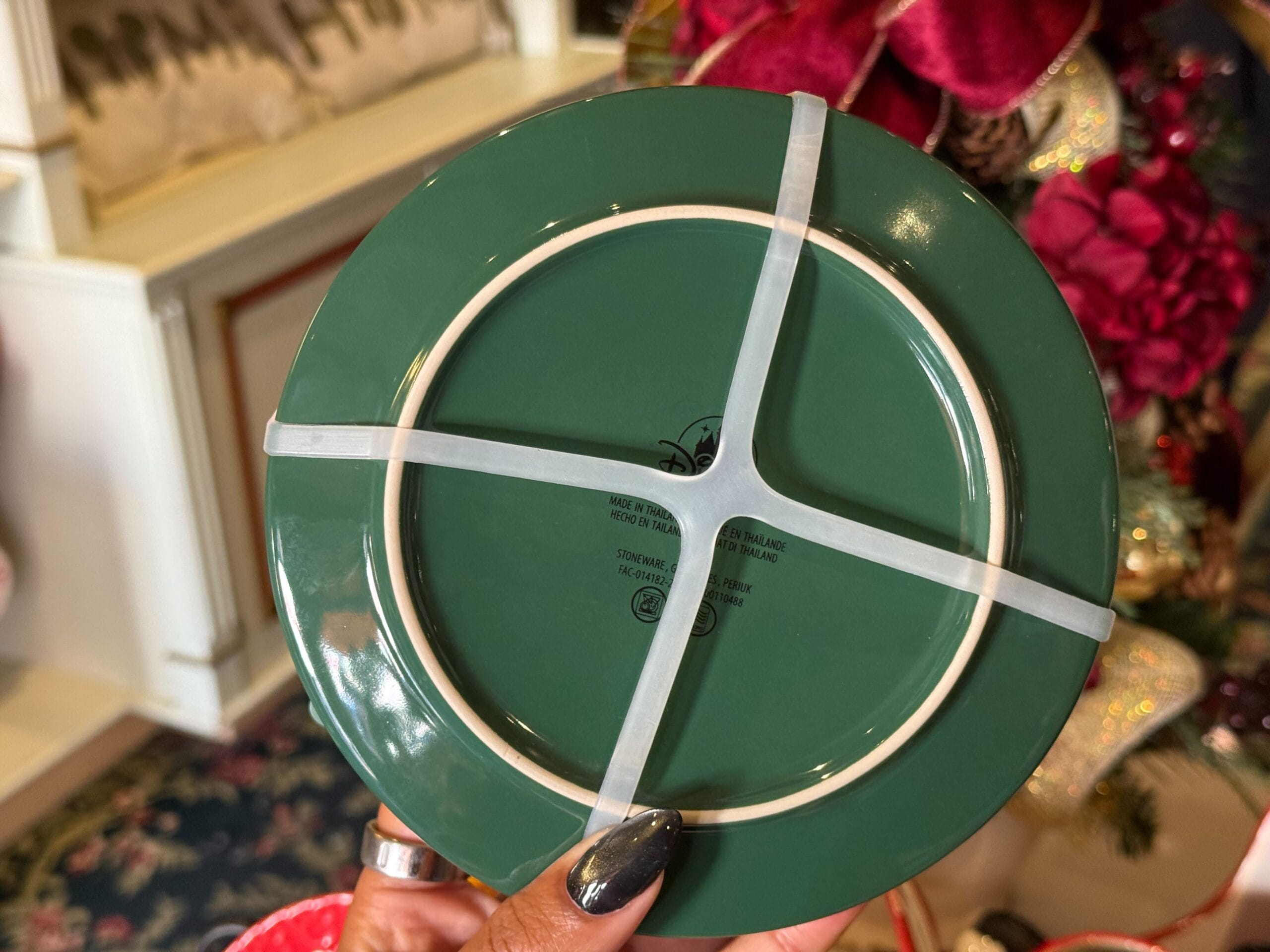 A hand holds a green plate with white bands, a cheerful Christmas item from Disneyland Resort—notable for its unique holiday designs.