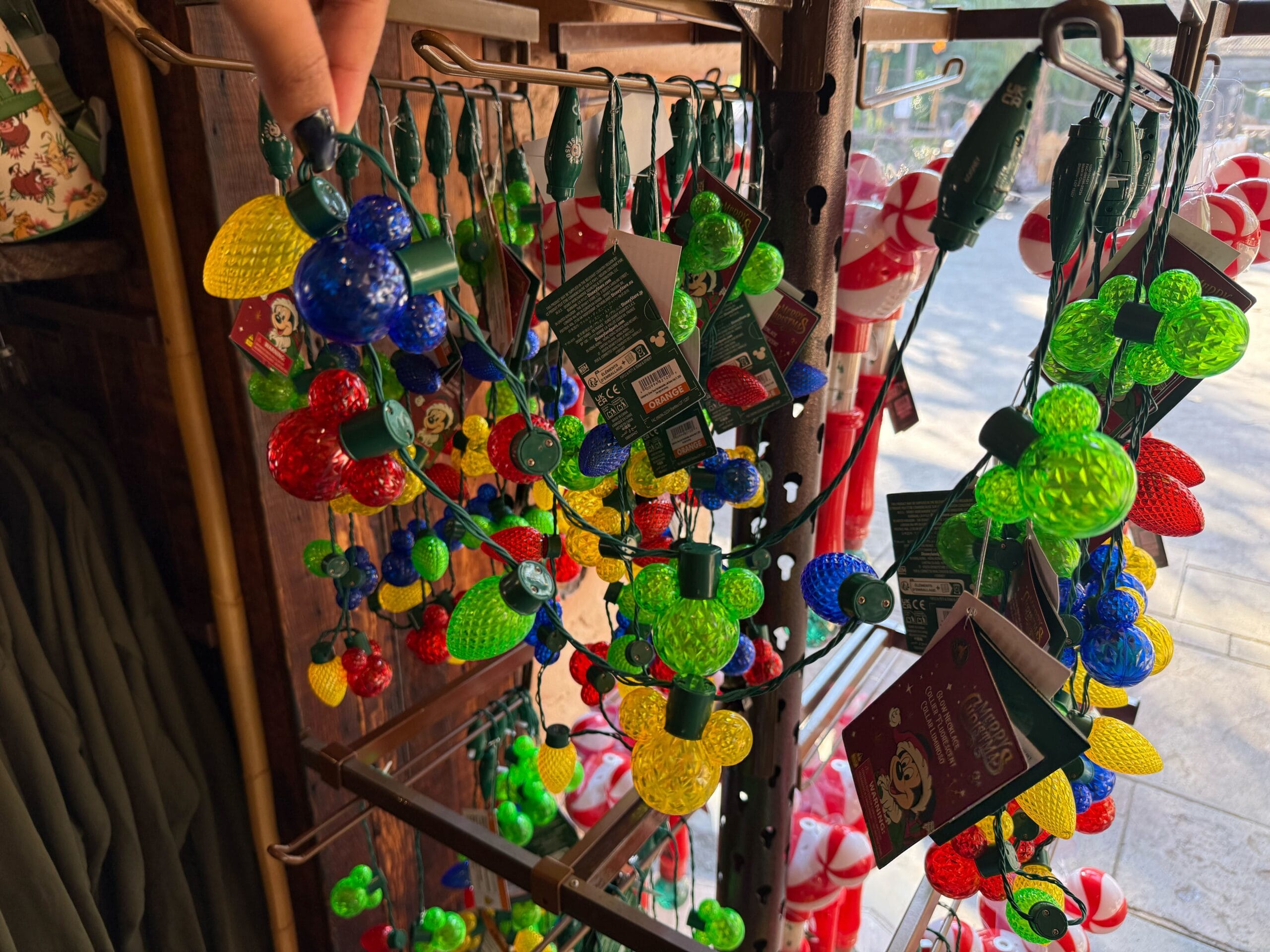 Mickey Mouse-shaped colorful holiday string lights sold as Christmas merchandise at Disneyland Resort, with Sleeping Beauty Castle nearby.