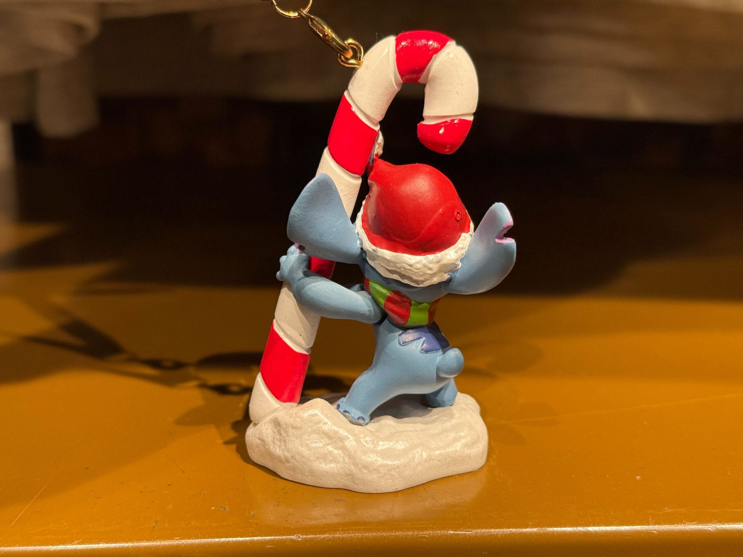 A small blue shark-like figurine hugging a candy cane on snow, festive Christmas merchandise seen at Disneyland Resort, not near any castle.