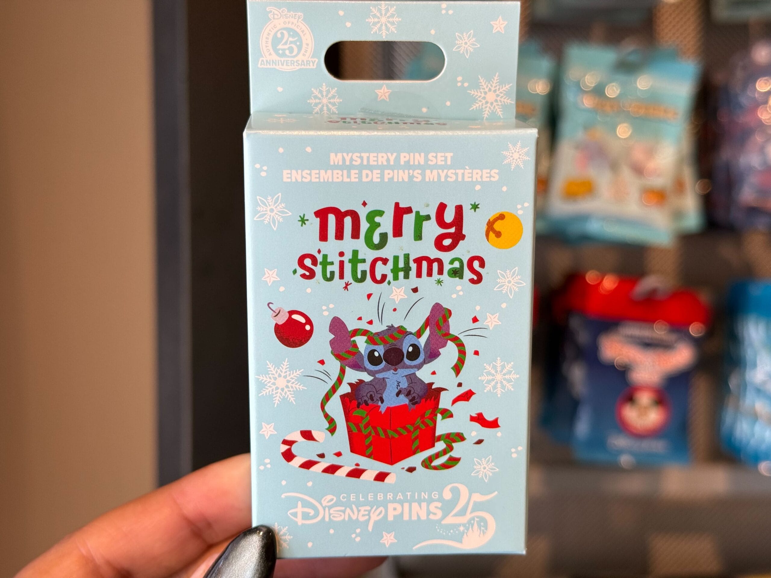 A hand displays Disneyland Resort Christmas merch—a Disney pin box featuring Stitch with "Merry Stitchmas" decor, perfect for fans.