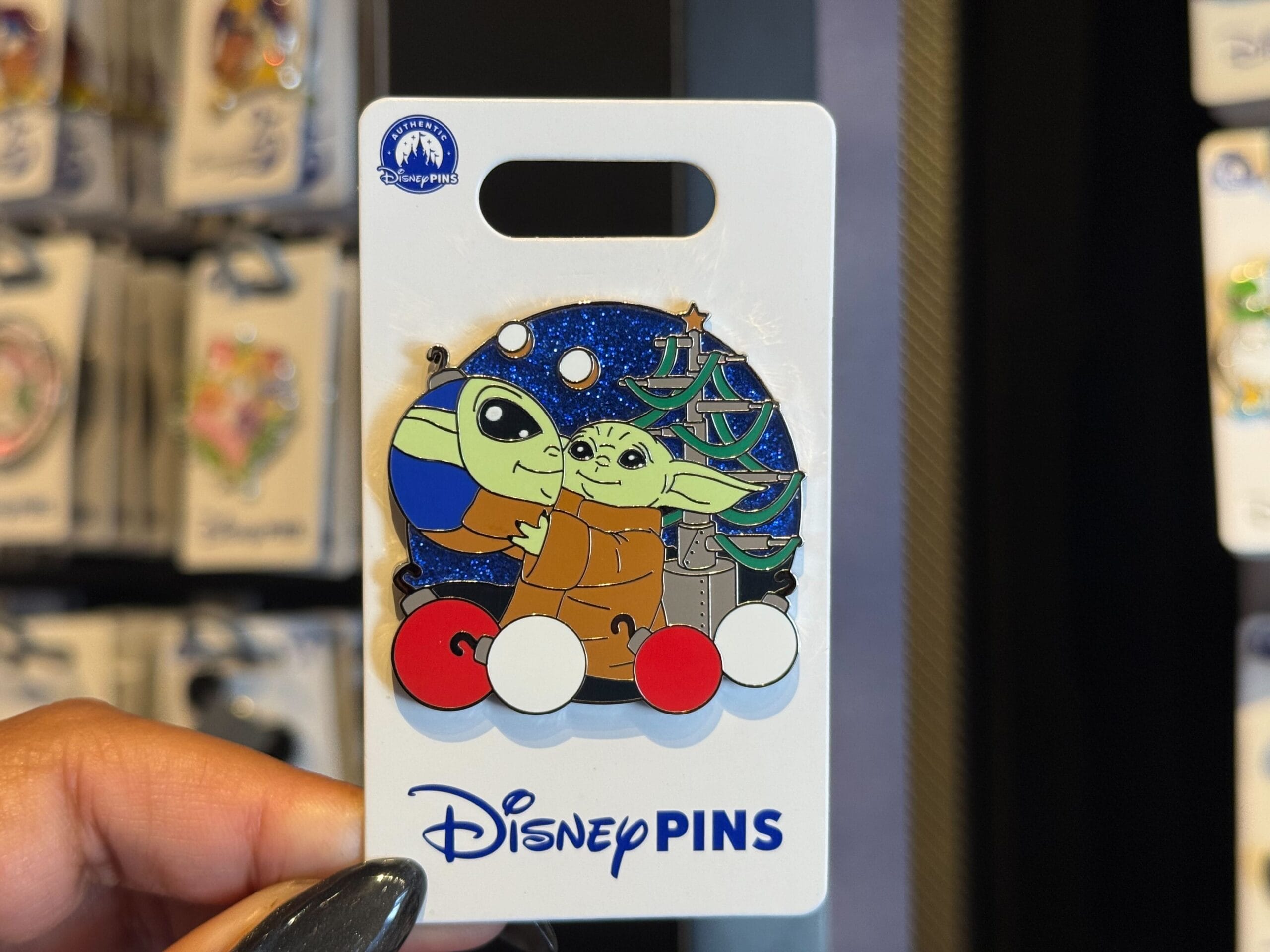A hand displays a Disneyland Resort pin of Grogu and a blue-green accented droid on a display card, exclusive to Disney Parks.