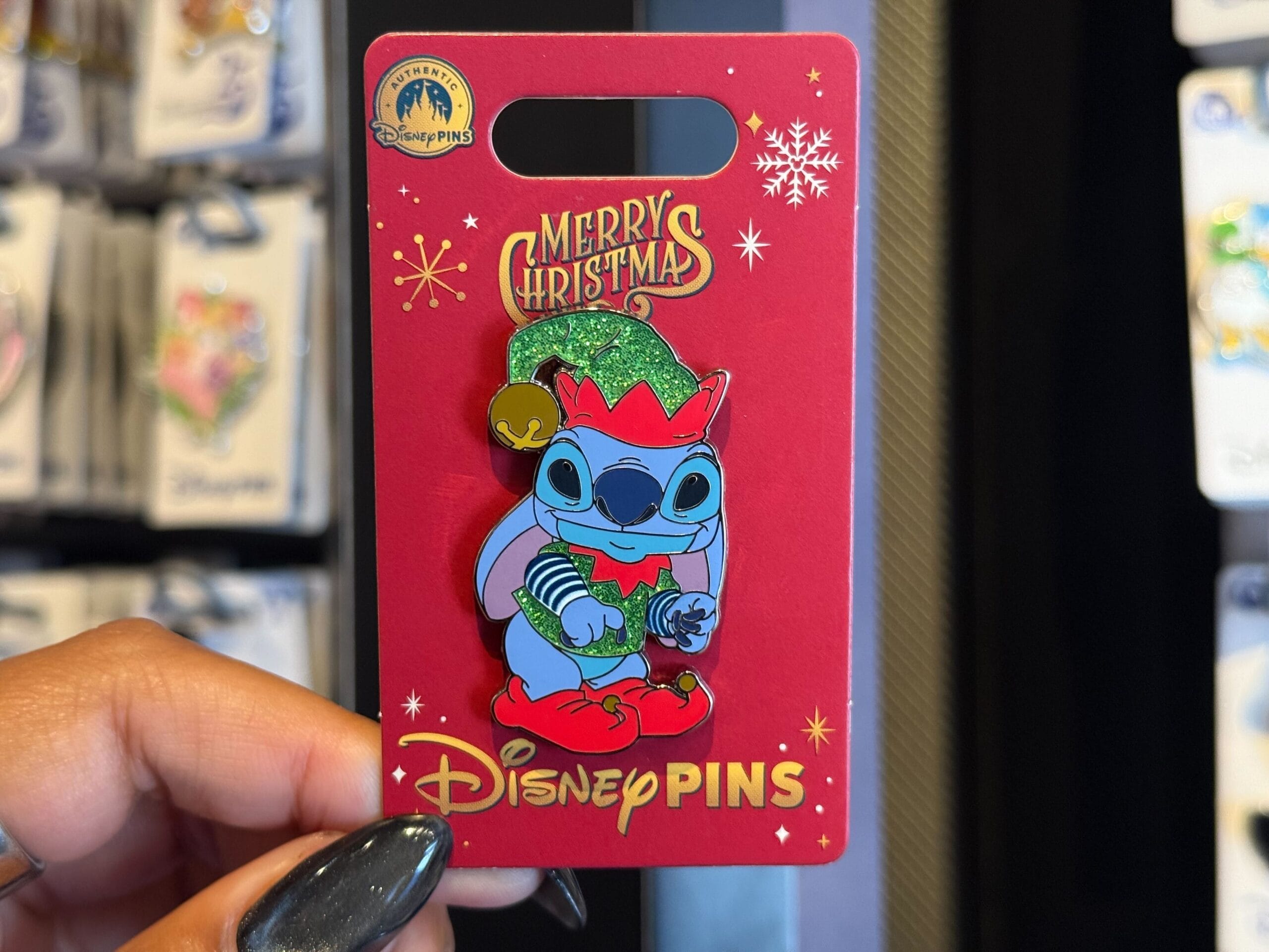 A hand displays Disneyland Resort Christmas merchandise—a Stitch-as-elf pin on a merry card, unique to U.S. Disney Parks.