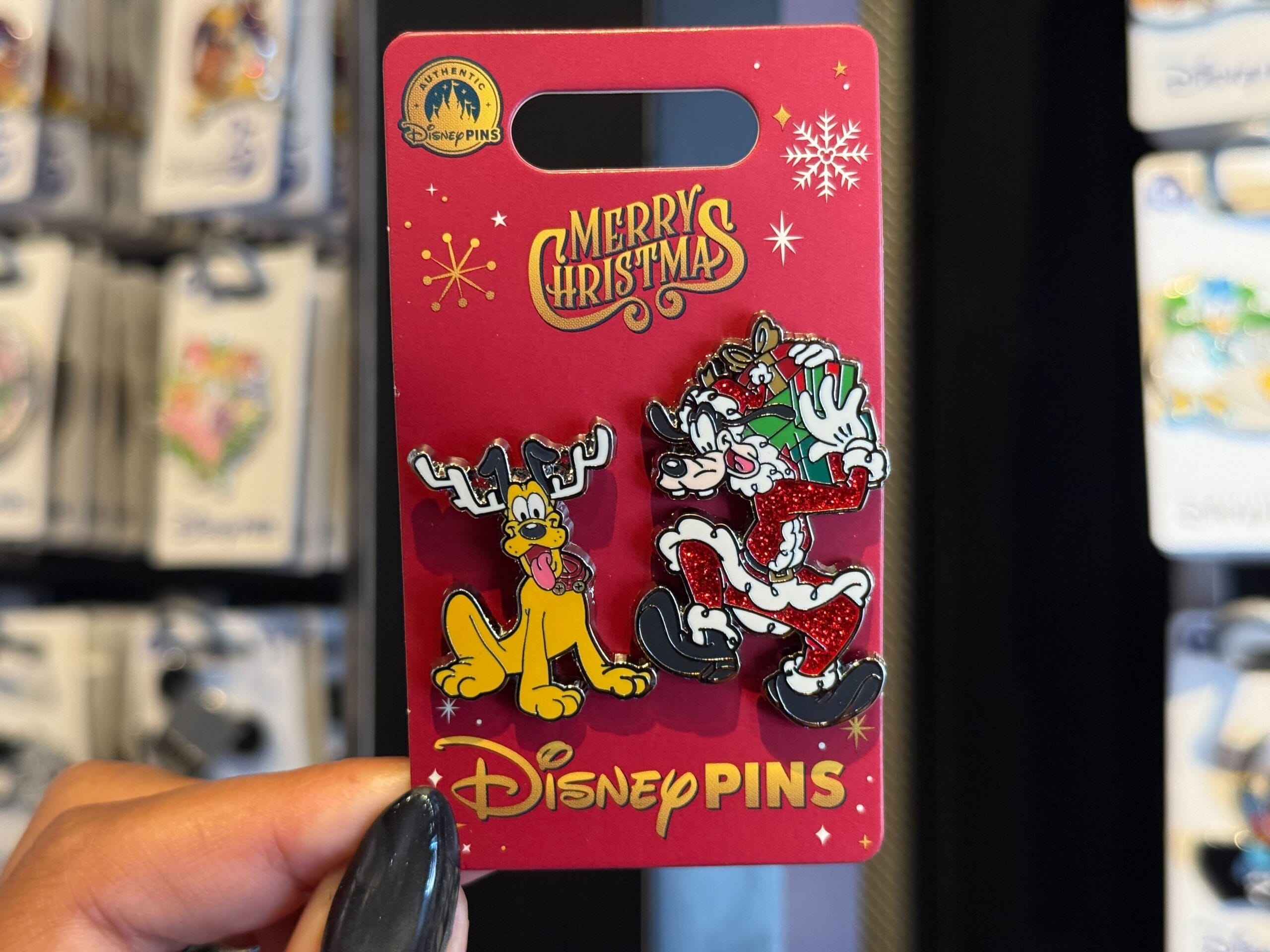 A hand displays a Disneyland Resort Christmas pin of Pluto as a reindeer and Goofy as Santa, set on red—classic Disneyland style.