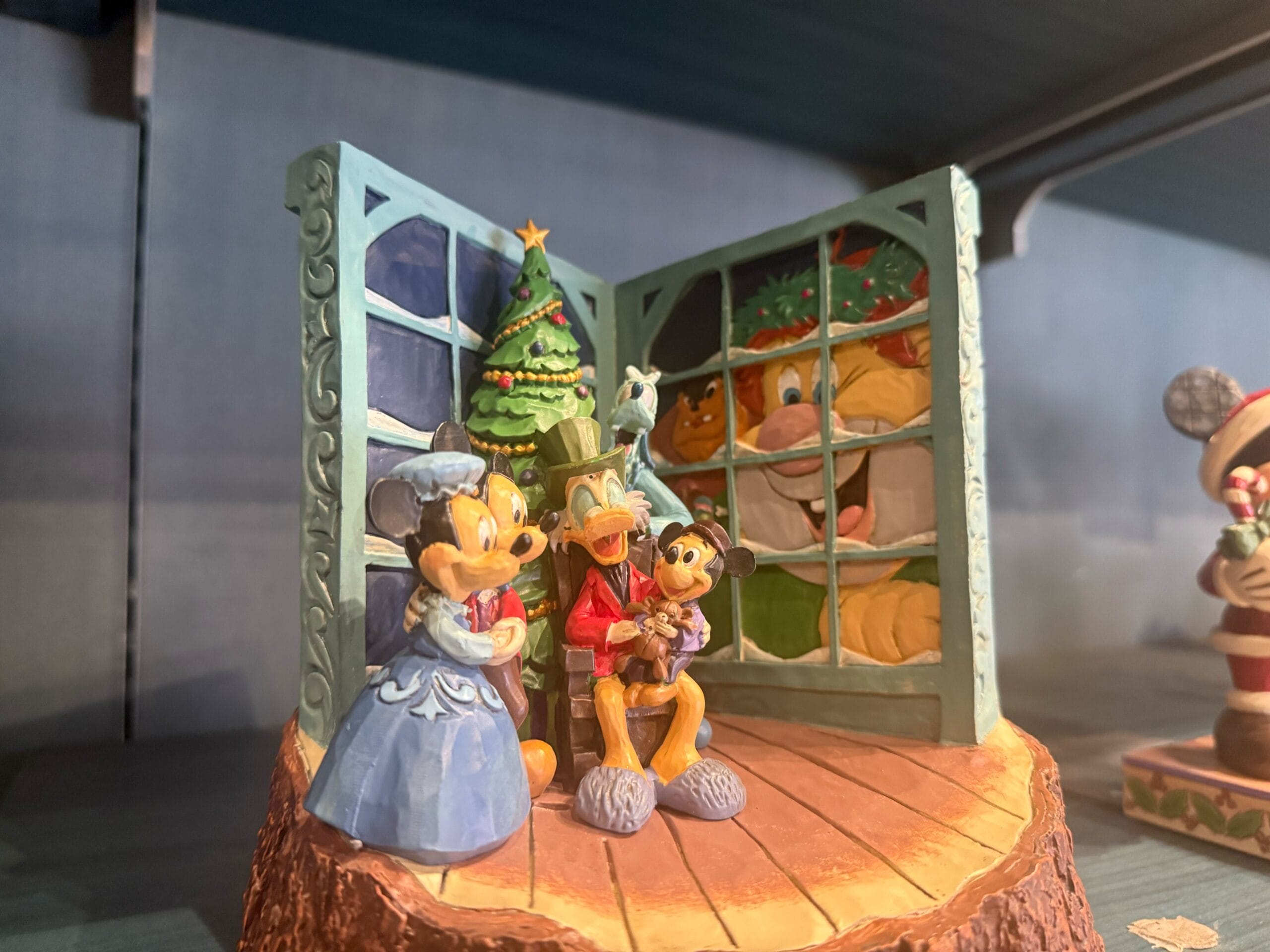 Disneyland Christmas merch: Minnie, Donald & Mickey in Victorian dress by festive tree and window, classic Disneyland holiday style.