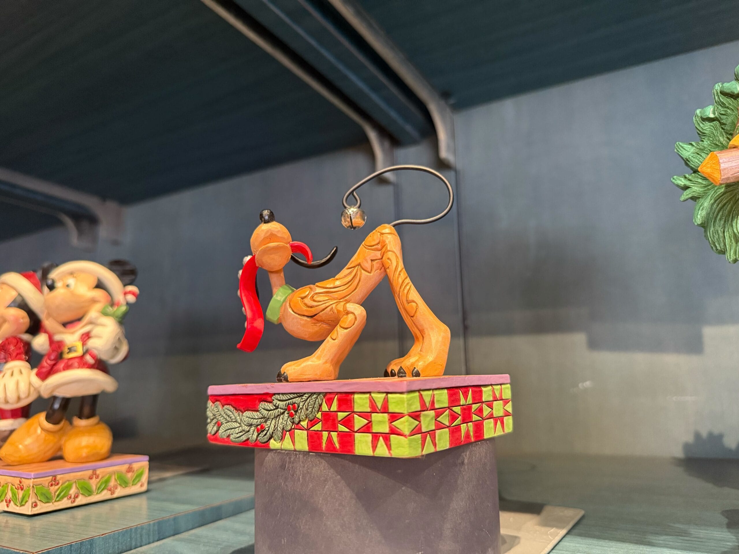 A festive Pluto figurine with a red scarf sits on a holiday-themed base, capturing the Disneyland Resort's Christmas spirit.