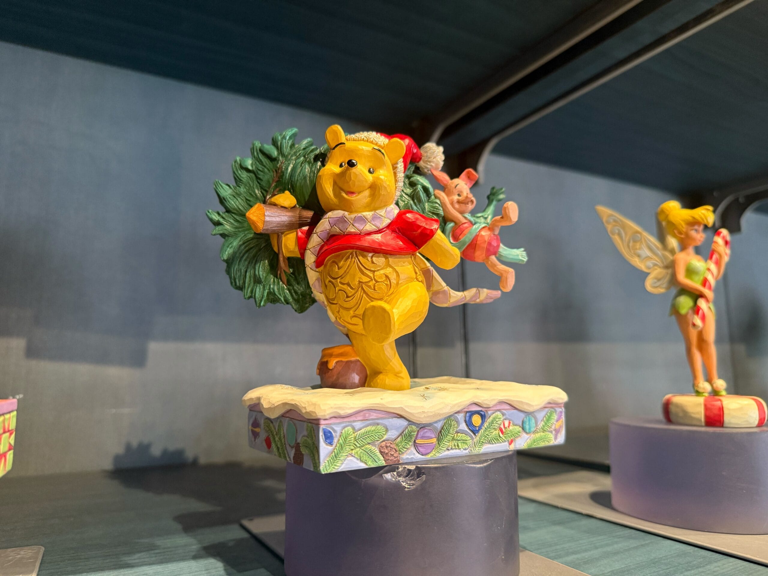 Winnie the Pooh and Piglet, dressed festively, carry a Christmas tree on a Disneyland Resort display—Sleeping Beauty Castle nearby.