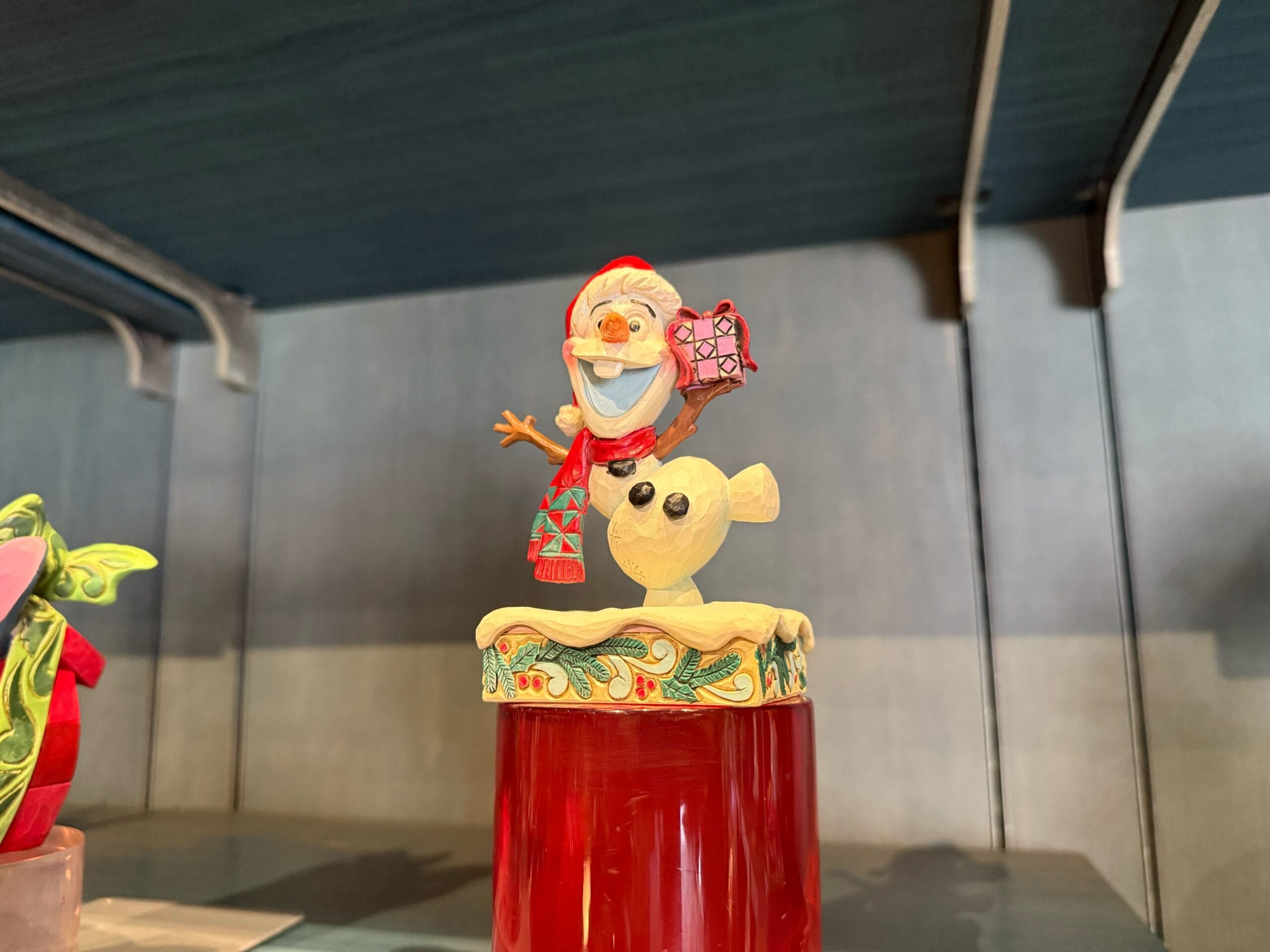 Olaf from Frozen, in a festive red hat and scarf, stands on a decorated base at Disneyland Resort—not pictured by any castle.